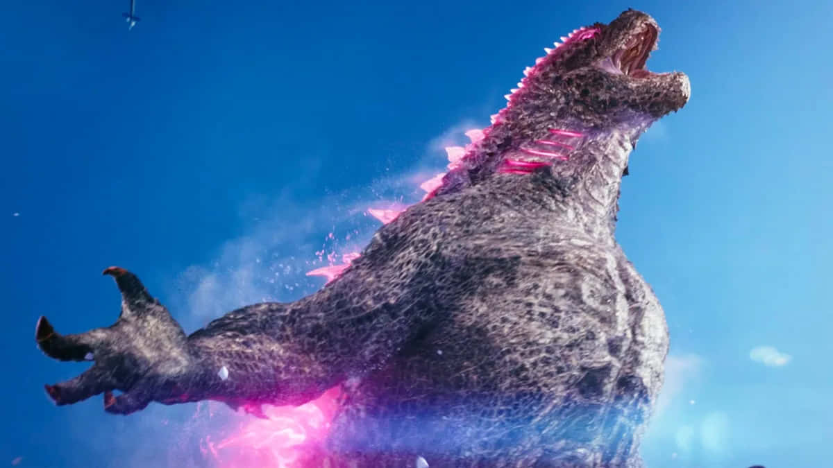 Godzilla X Kong The New Empire 桌布 壁紙 — 一隻巨大的哥吉拉對著晴朗的藍天咆哮，粉紅色的能量沿著牠的脊椎劈啪作響並從胸口噴發出來。