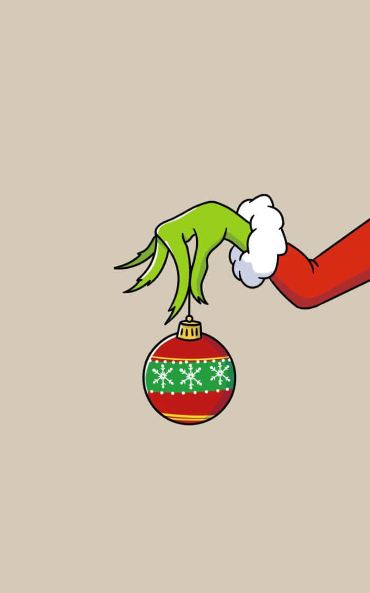  壁紙 — 一隻綠色聖誕怪傑的手，穿著紅色袖子，在米色背景上拿著一個紅色和綠色的雪花裝飾品。