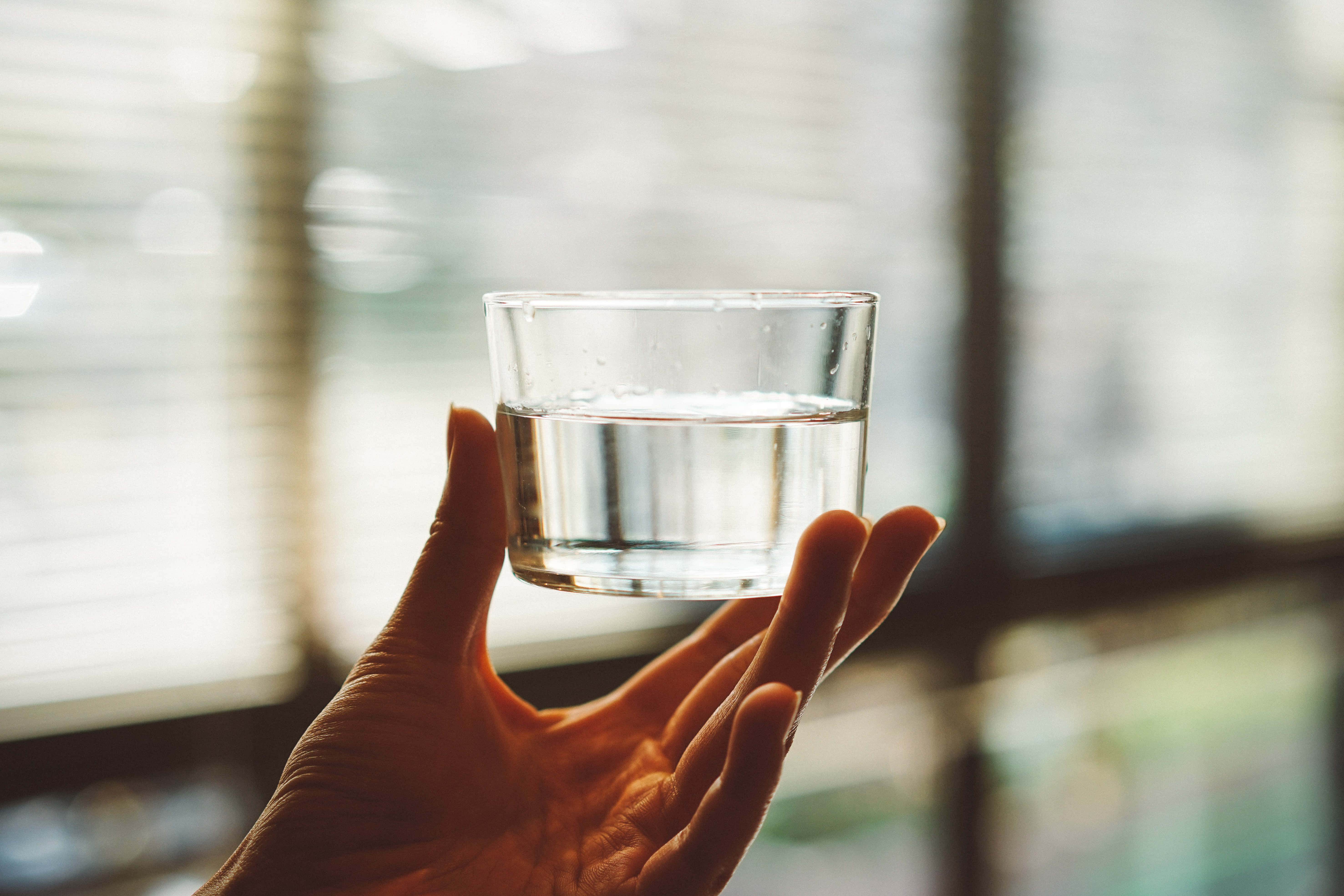 Hydration 桌布 壁紙 — 一隻手輕輕拿著一杯清水，背景是柔和模糊的窗戶。