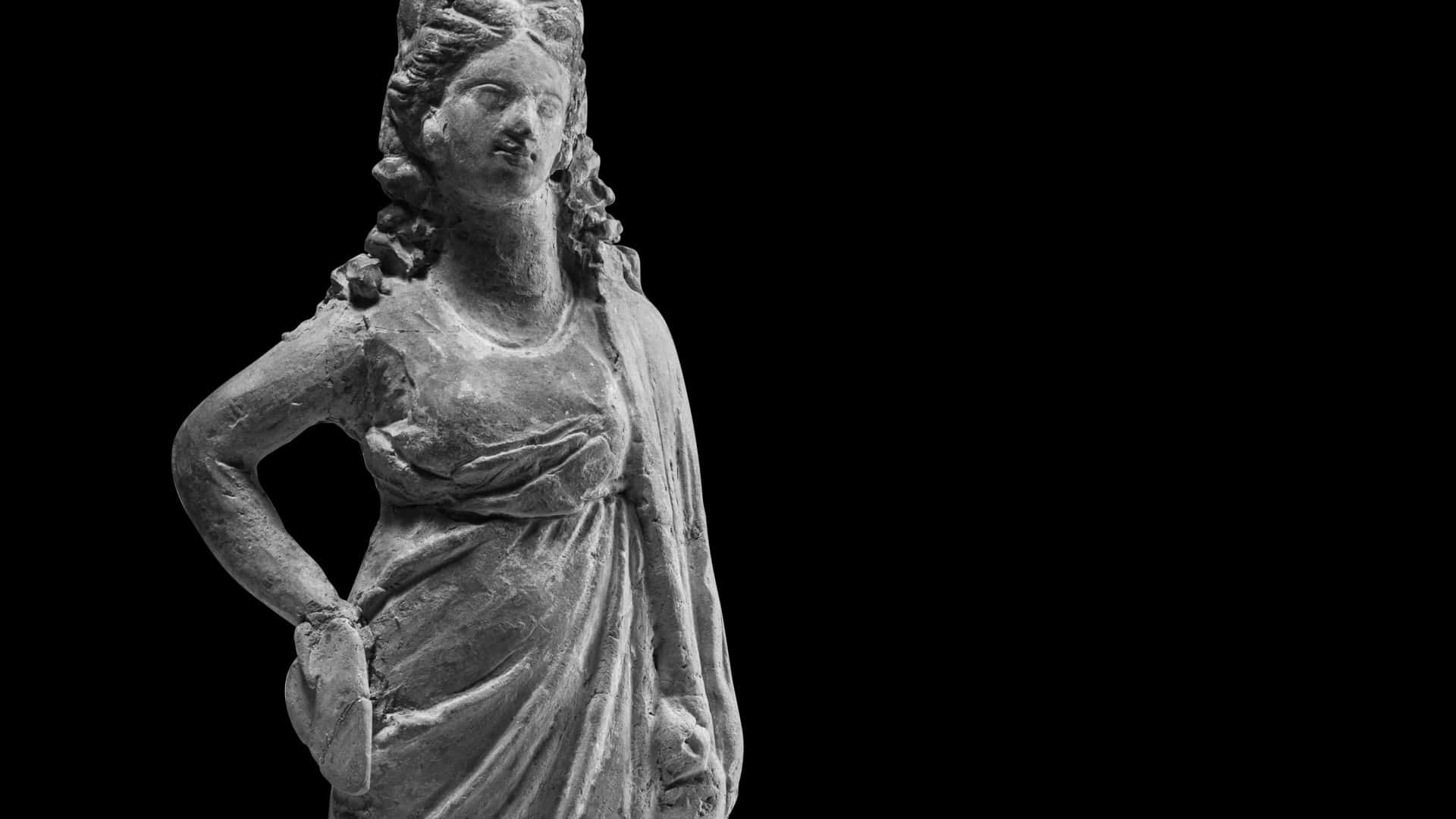  壁紙 — 一尊風化的古代女性雕像，身披垂褶布料，在純黑背景前以鮮明的單色呈現。