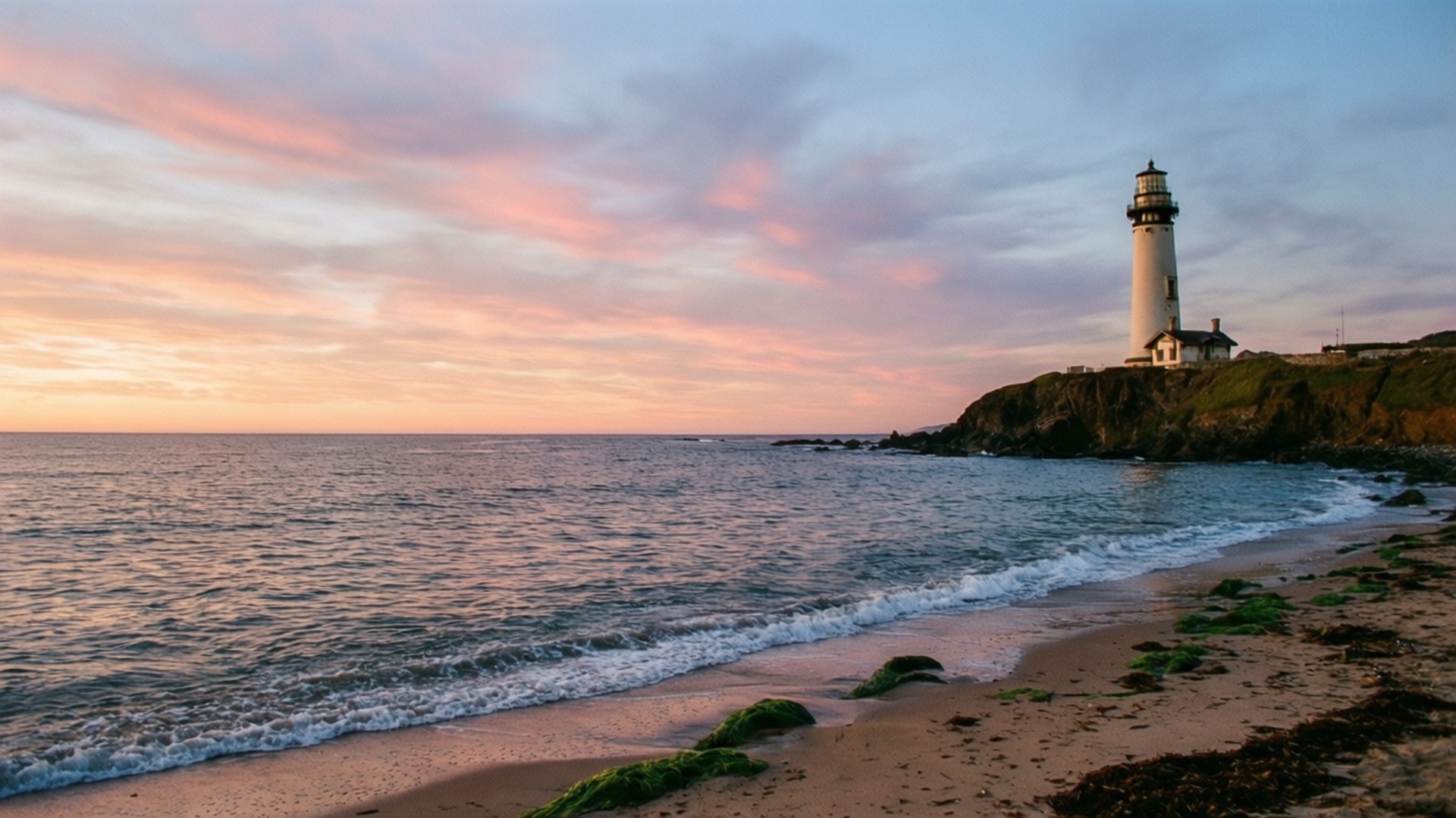 Lighthouse Horizon 壁紙 — 一座白色燈塔矗立在岩石懸崖上，夕陽將粉紅色和橙色的色調投射在海洋和天空上。