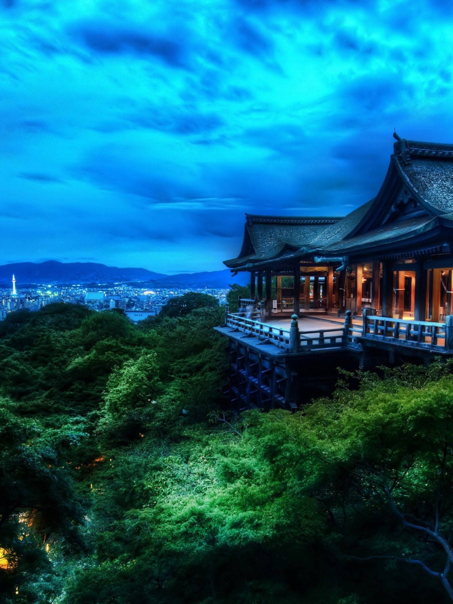 山頂寺廟在暮色中俯瞰城市，藍天綠樹 — iPad 壁紙