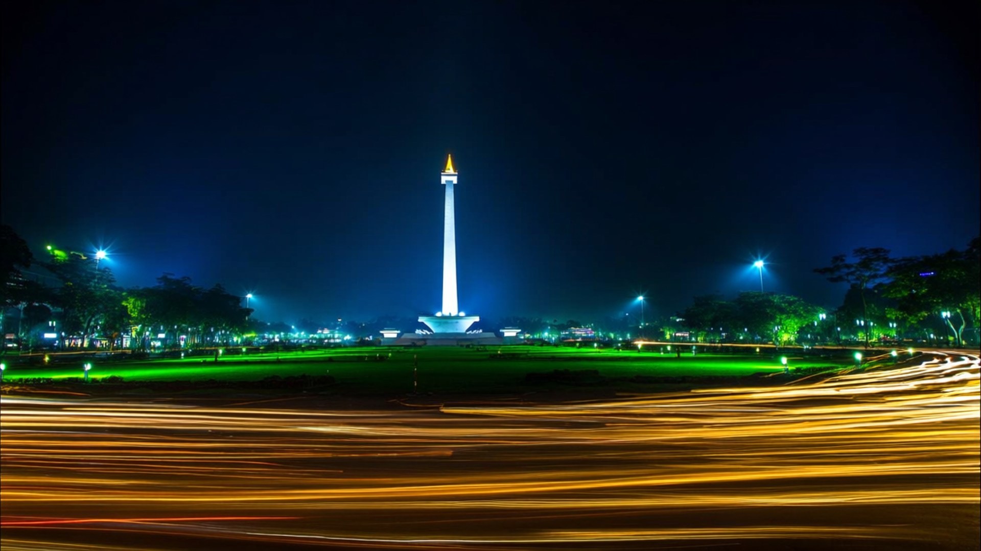 Monas Night Lights 壁紙 — 一座高聳的紀念碑在夜空下發出白光，金色光跡掠過前景的草地。