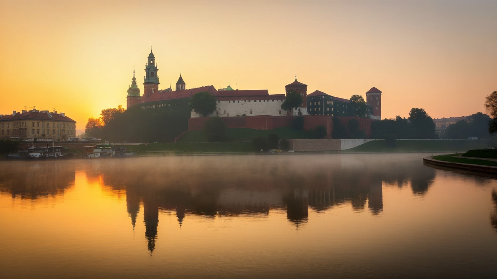 Wawel Castle Sunrise 壁紙 — 一座歷史悠久的城堡，紅牆尖塔倒映在平靜的水面上，金色的晨光以溫暖的色調沐浴著場景。