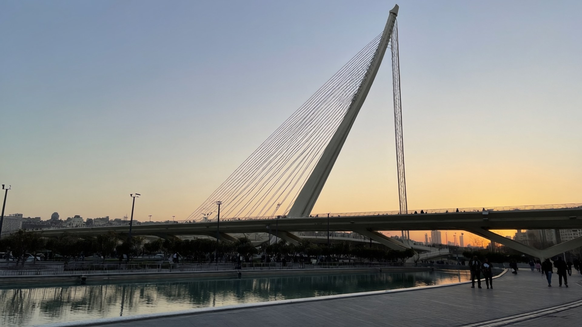 Tabiat Bridge Sunset 壁紙 — 一座現代斜張橋在日落時分橫跨平靜的水道，有剪影行人及漸層天空。
