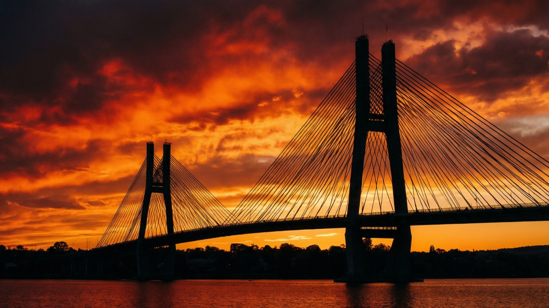 Commonwealth Bridge Sunset 壁紙 — 一座斜張橋在平靜水面上倒映著火紅橙色的日落天空的剪影。