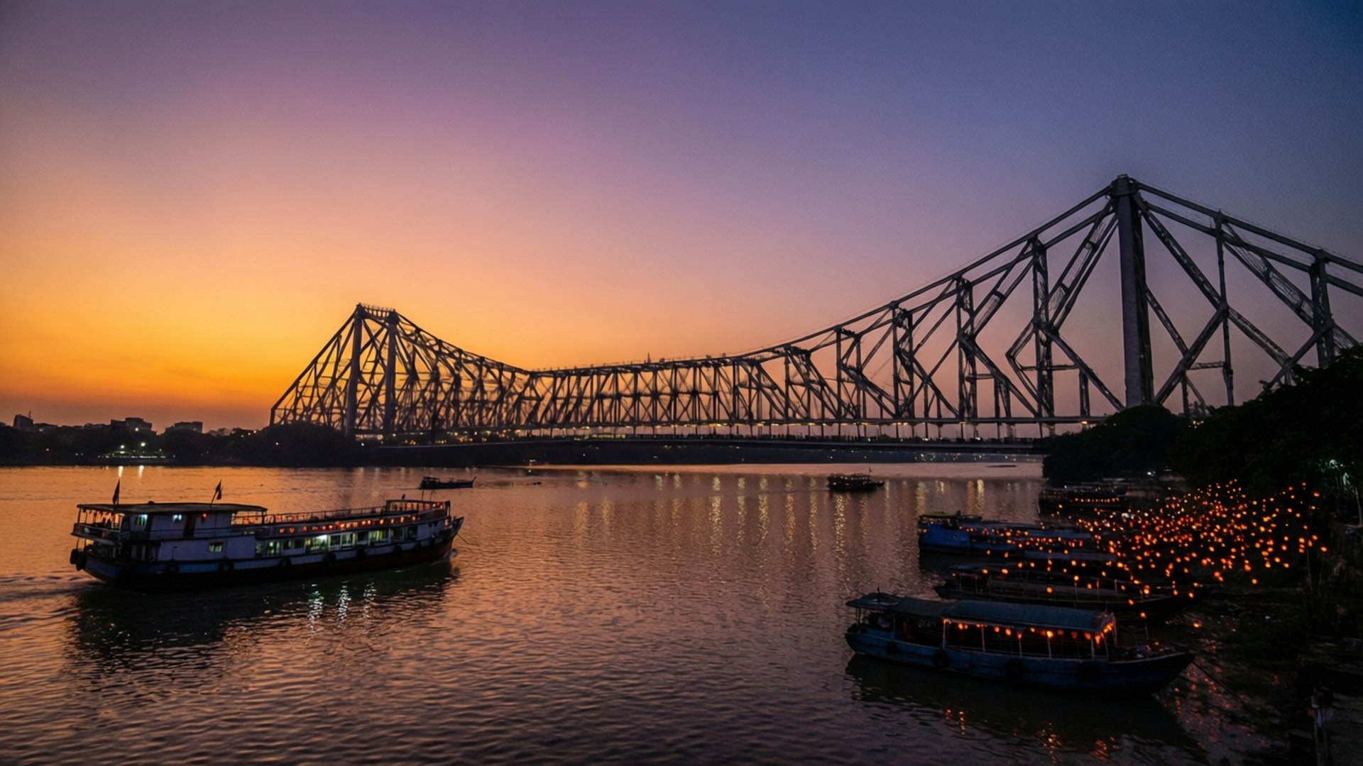 Dusk Over Hooghly 壁紙 — 一座雄偉的鋼桁架橋在黃昏時跨越河流，船隻在溫暖燈光下閃耀，襯著漸變的天空。