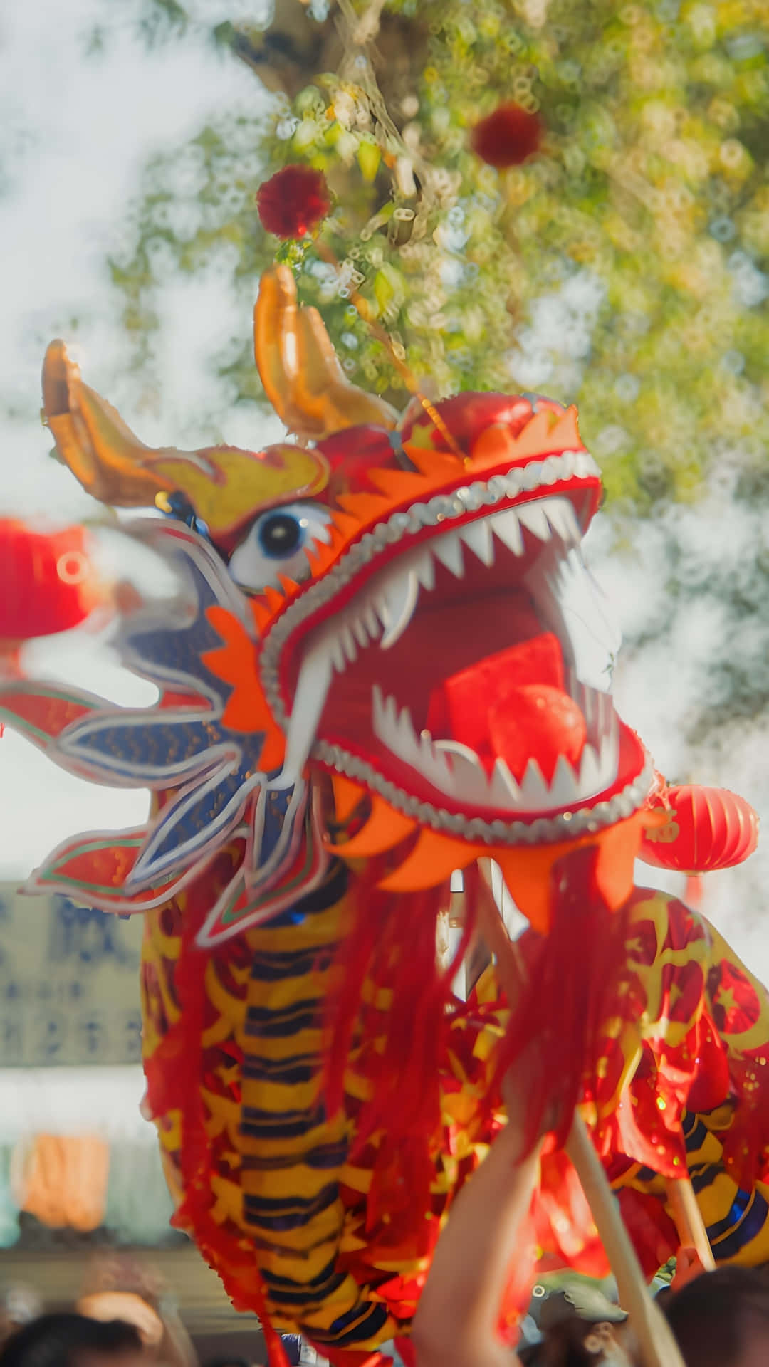  壁紙 — 一件鮮豔的紅金色舞龍服裝，帶有鋒利的牙齒和飄逸的絲帶，在節日戶外慶祝活動中被高高舉起。