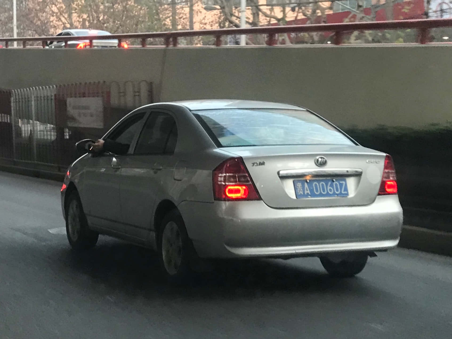 壁紙 — 一輛銀色轎車在黃昏時分行駛於城市道路，在天橋下煞車燈亮起。