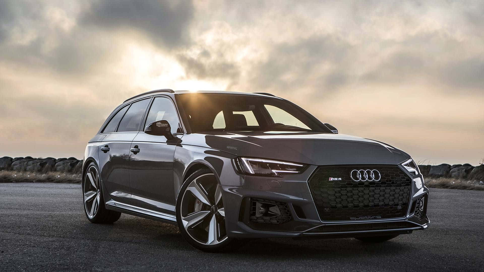 Audi Rs4 桌布 壁紙 — 一輛時尚的灰色奧迪 RS4 Avant 旅行車在開闊的道路上，在戲劇性的日落光線下閃閃發光。