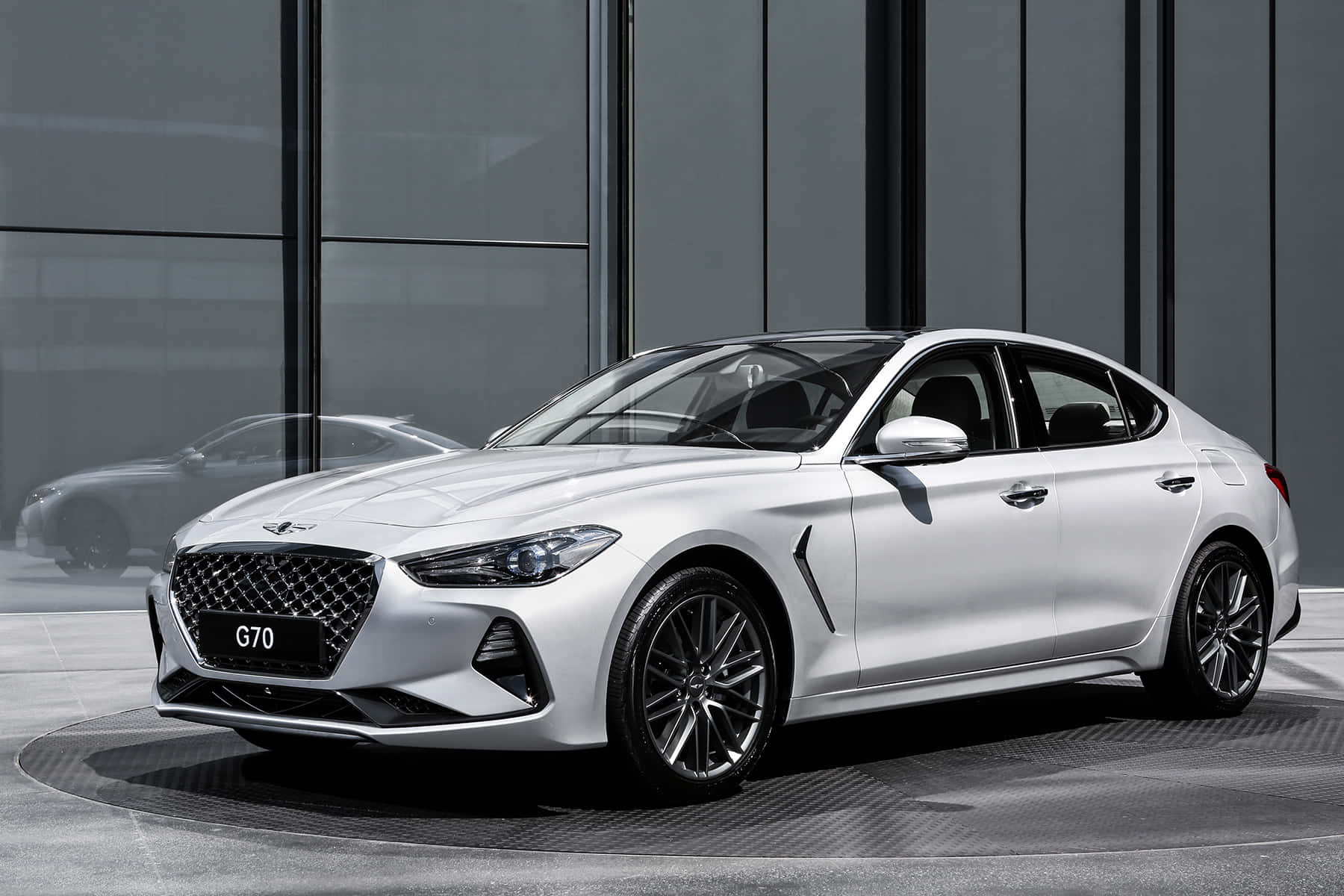Genesis G70 桌布 壁紙 — 一輛時尚的白色Hyundai G70轎車在現代玻璃和鋼鐵背景前，於攝影棚燈光下閃閃發光。