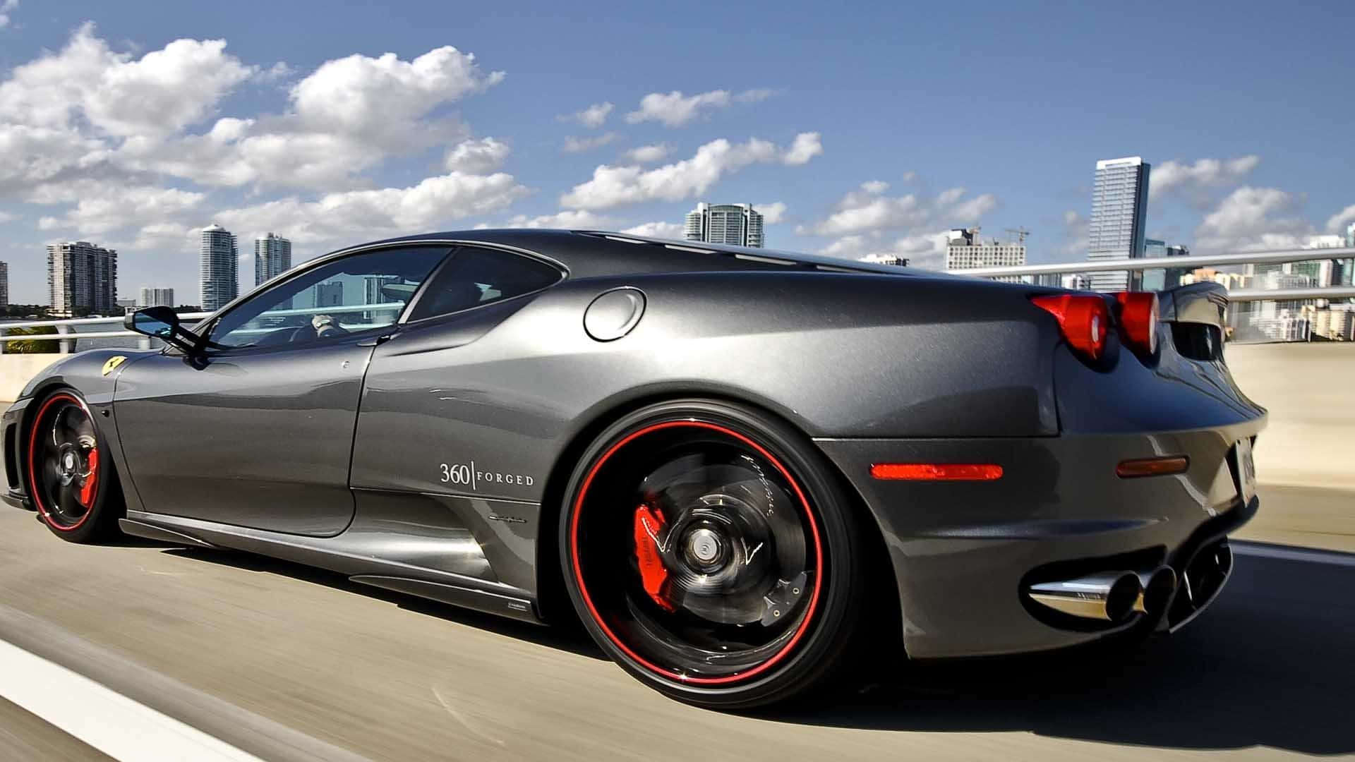 Fantasy Cars 桌布 壁紙 — 一輛流線型消光灰色法拉利 360 Forged 在晴朗藍天白雲下的城市高速公路上疾馳。