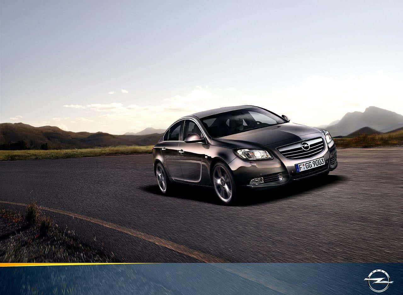 Opel Insignia 桌布 壁紙 — 一輛時尚的深灰色轎車在柔和的金色日落天空下行駛在蜿蜒的山路上。