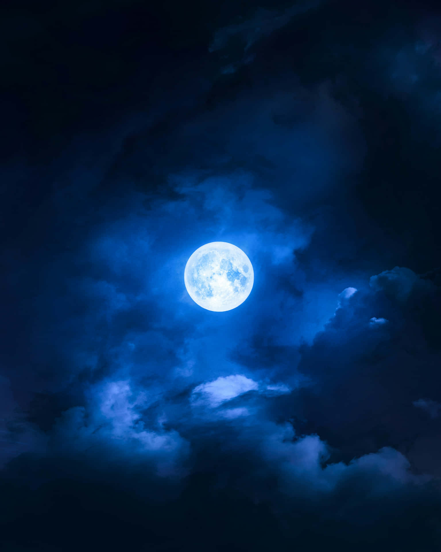  壁紙 — 一輪明亮的滿月在深邃的夜空中穿過旋轉的深藍色雲層發光。