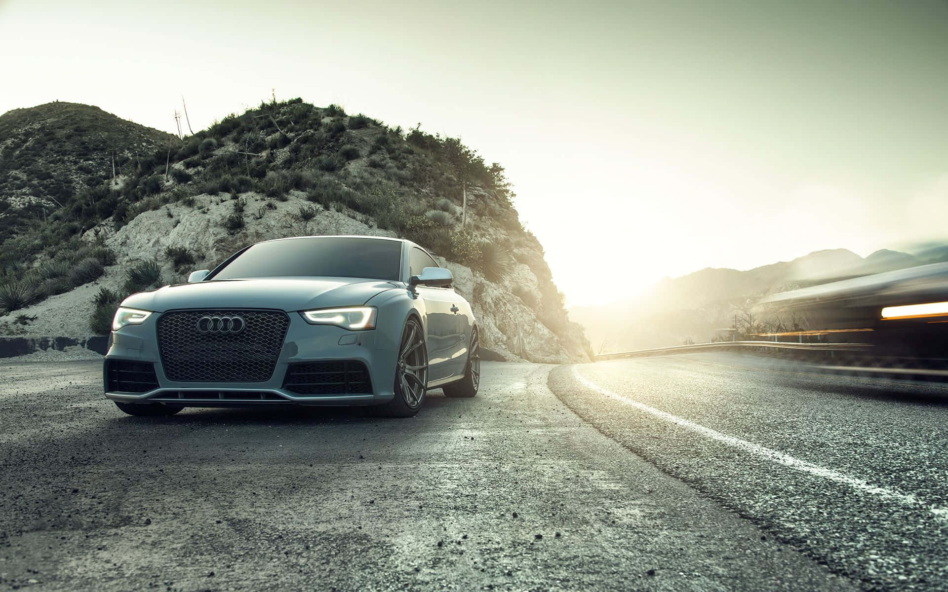 Audi S5 桌布 壁紙 — 一輛時尚的銀色奧迪跑車在蜿蜒的山路上停下，夕陽在遠山後閃耀。