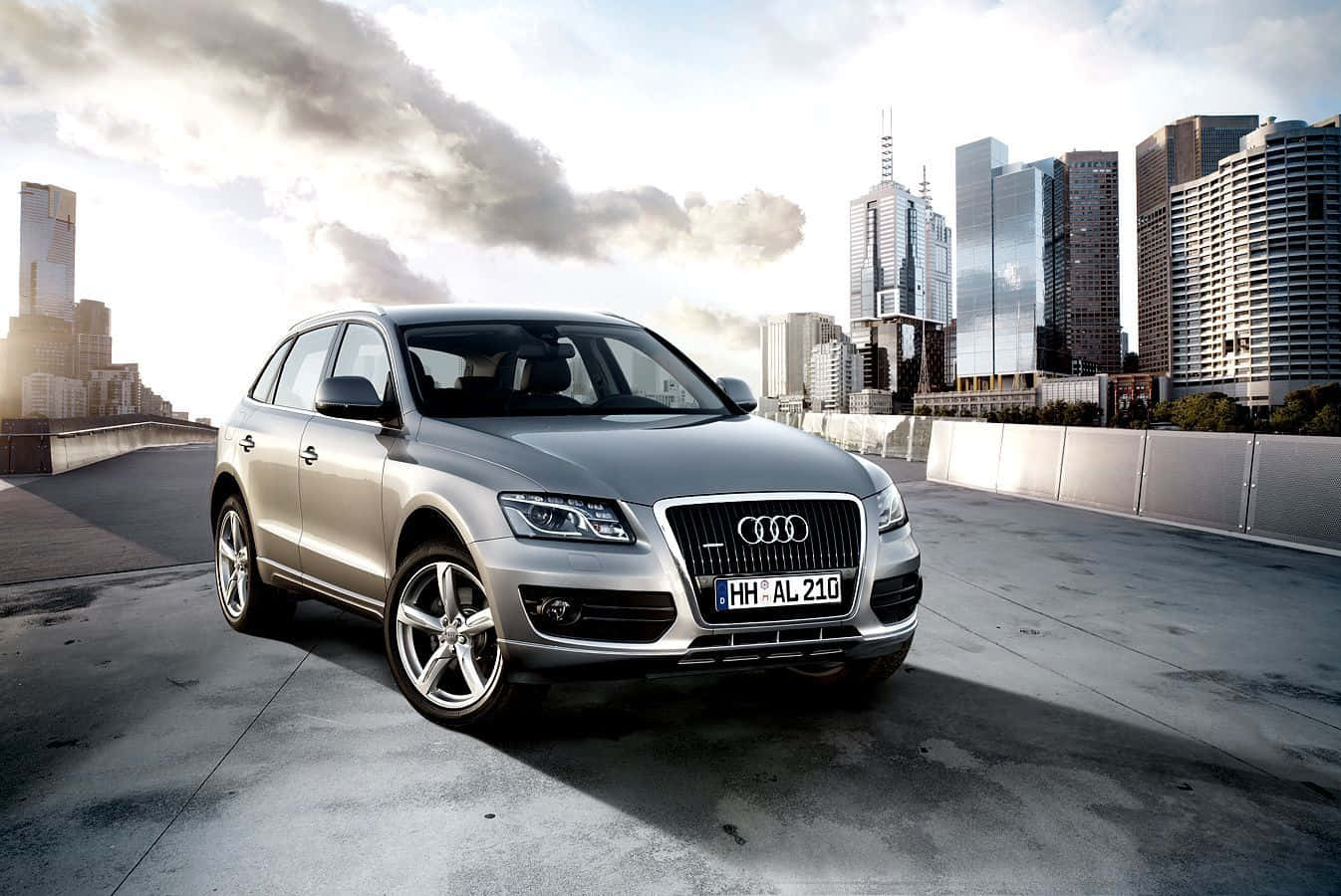 Audi Q5 桌布 壁紙 — 一輛時尚的銀色奧迪Q5 SUV停放在混凝土高架橋上，背景是現代城市天際線和戲劇性的雲層。