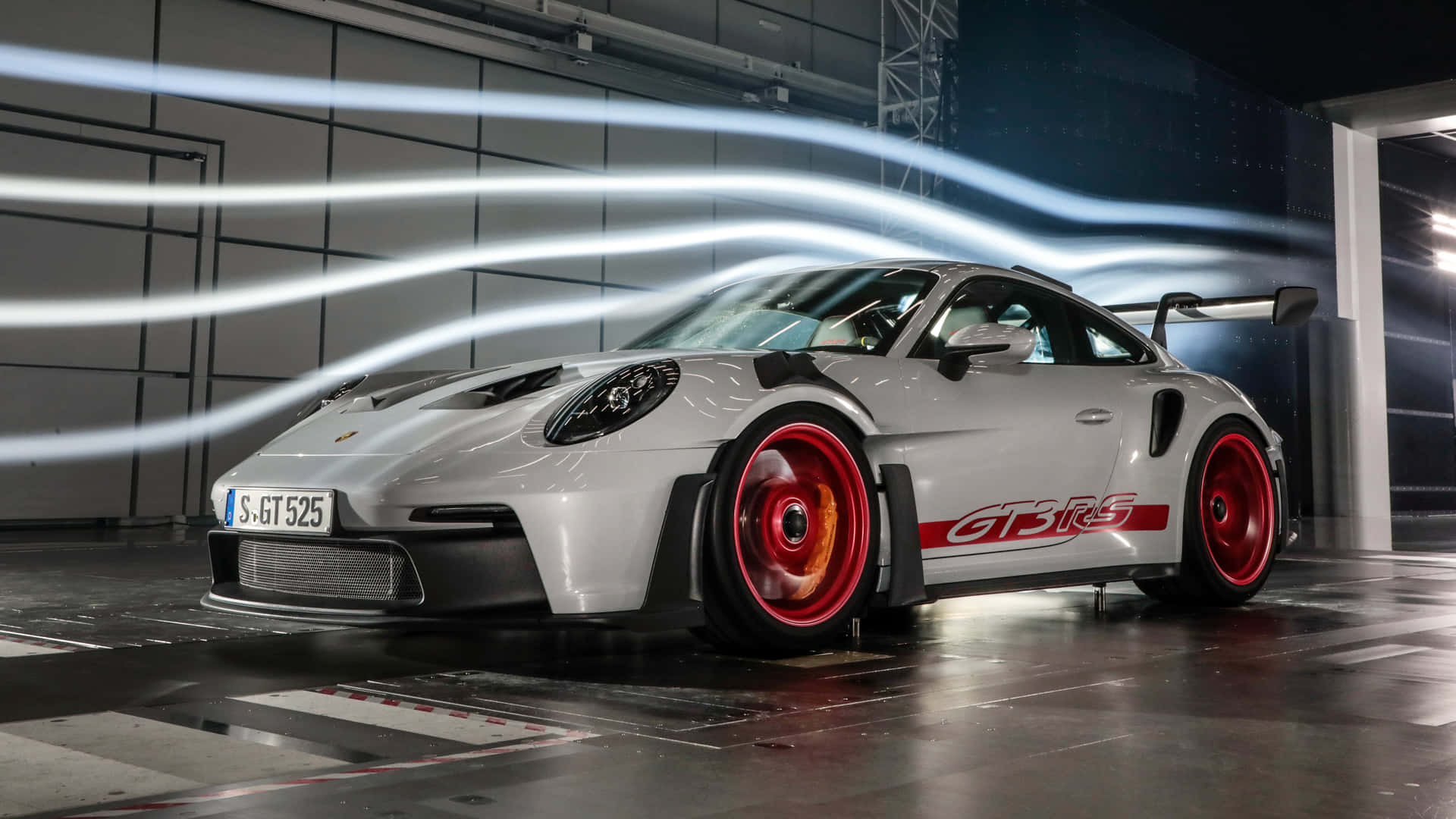  壁紙 — 一輛銀色保時捷911 GT3 RS，配備紅色輪圈和空氣動力學尾翼，在一個帶有發光氣流線條的高科技車庫中展示。