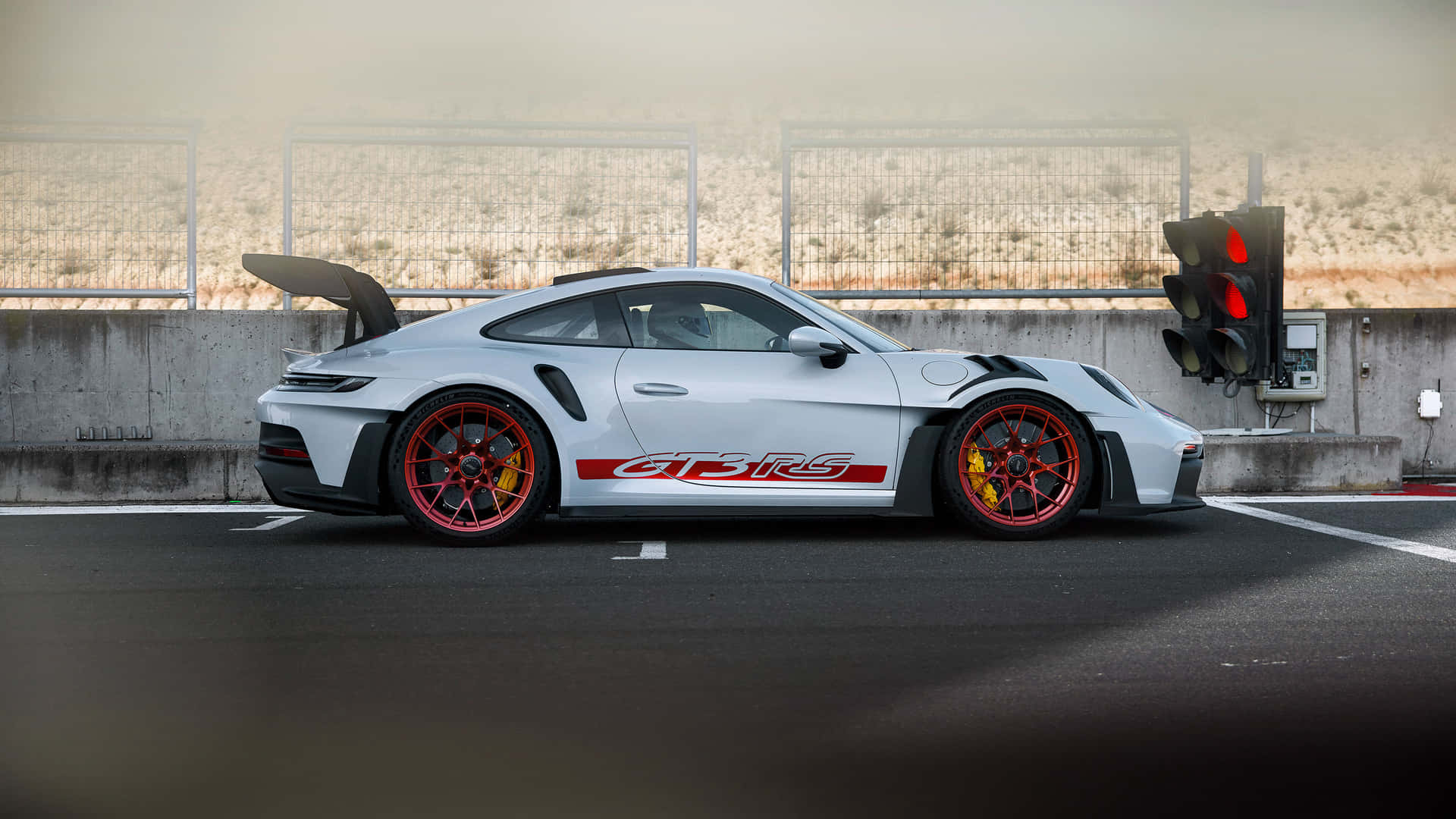  壁紙 — 一輛銀色保時捷911 GT3 RS，帶有紅色點綴和黃色制動卡鉗，在朦朧的日光下停在賽道交叉口。
