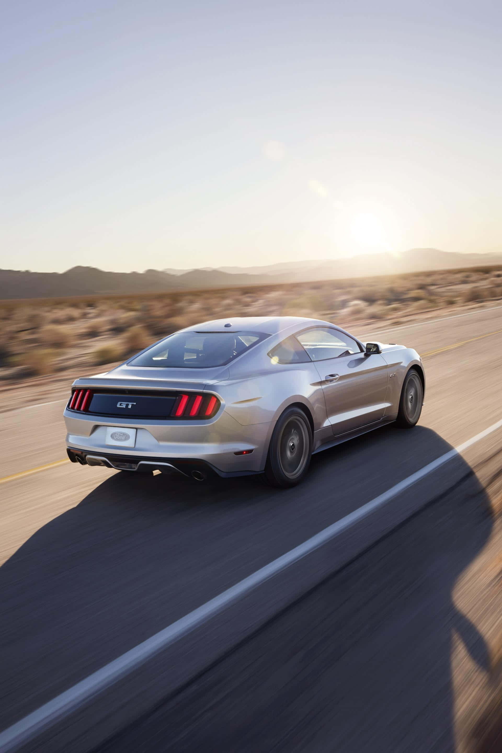 Ford Mustang California Special 桌布 壁紙 — 一輛銀色福特Mustang GT在日落時分於沙漠高速公路上飛馳，在金色光芒下投下長長的影子。