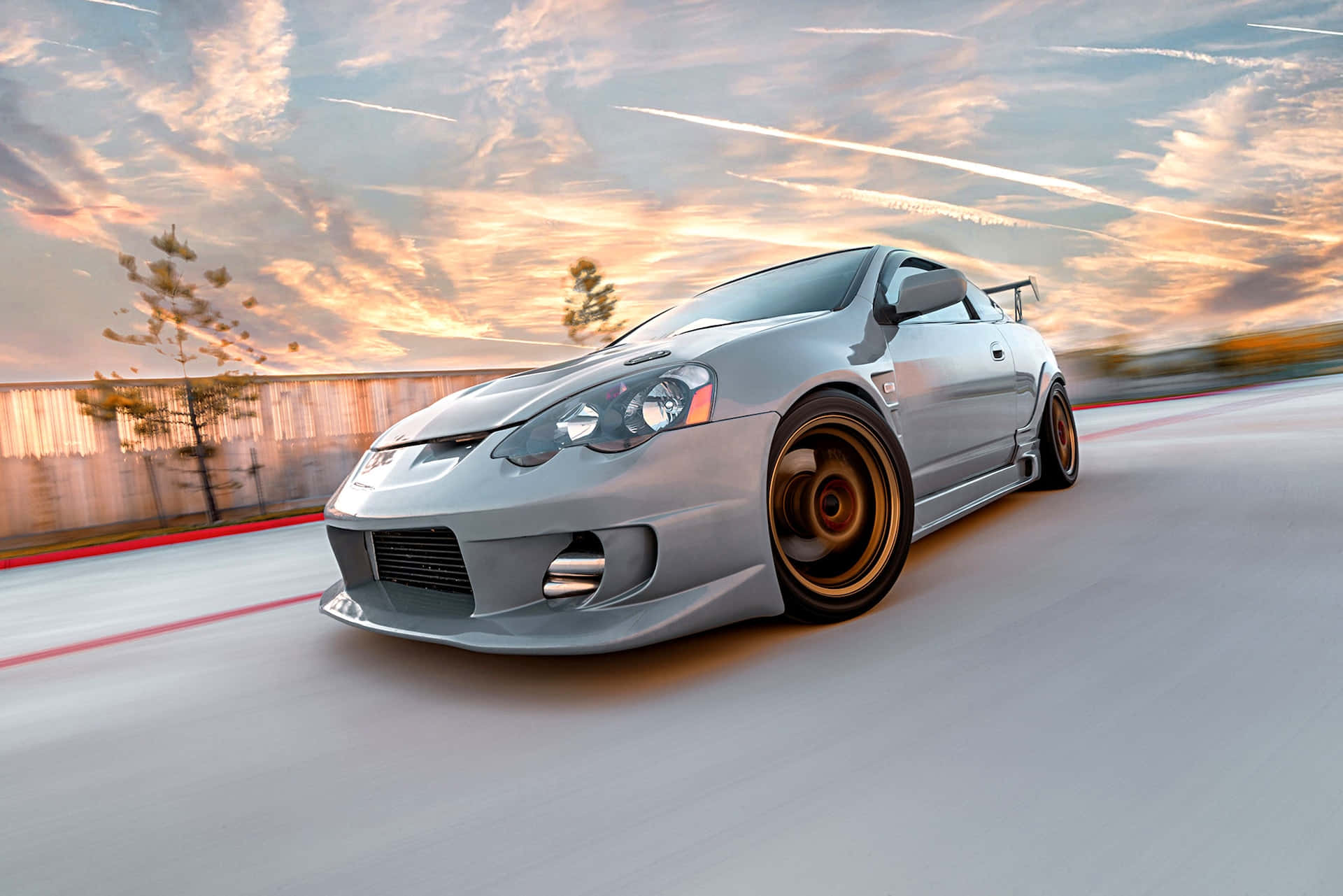 Acura Rsx 桌布 壁紙 — 一輛銀色改裝跑車在日落時分沿著賽道疾馳，帶有動態模糊和鮮豔的橙色雲彩。