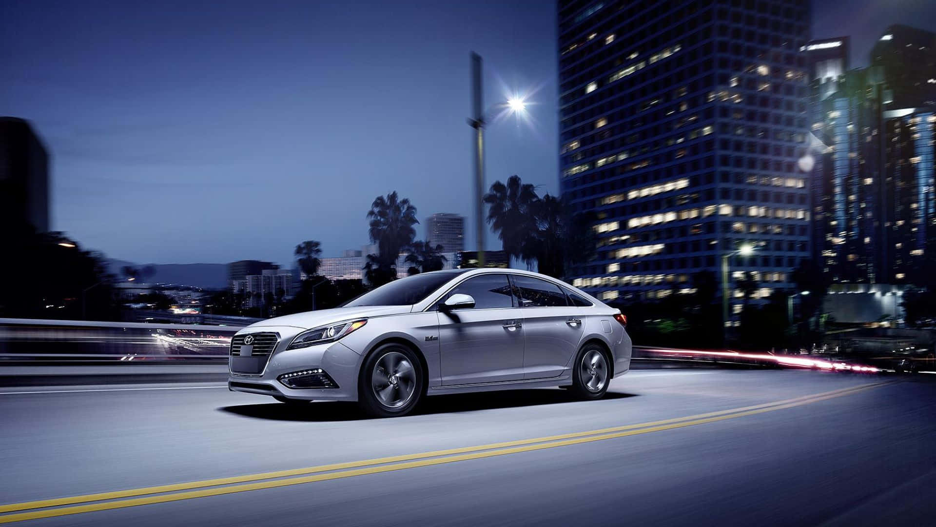 Hyundai Sonata 桌布 壁紙 — 一輛銀色轎車在夜間高速駛過城市，模糊的燈光掠過高樓大廈和棕櫚樹。