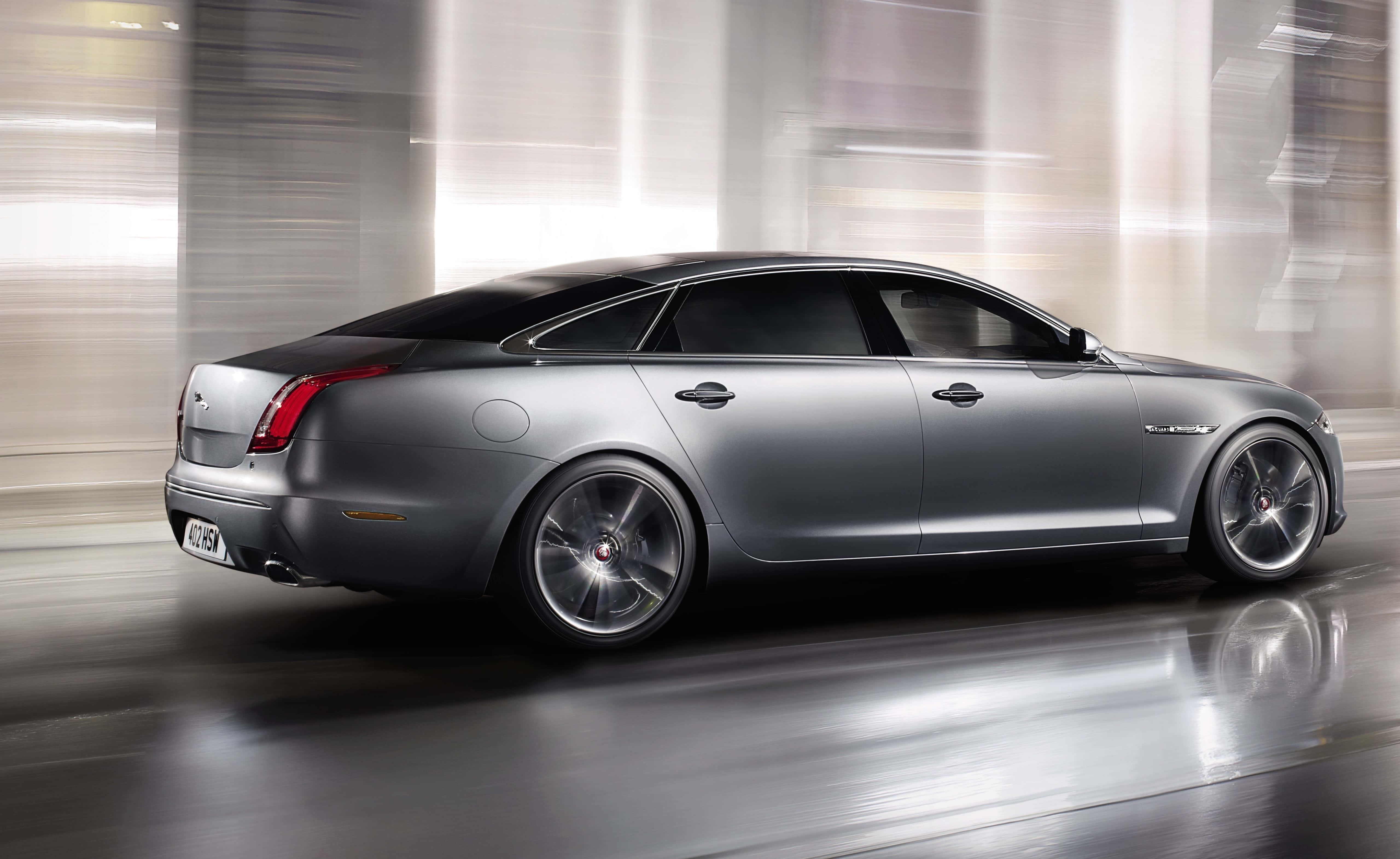 Jaguar Xjr 桌布 壁紙 — 一輛流線型的銀色積架轎車穿過模糊的城市隧道，動態模糊強調了速度和奢華。