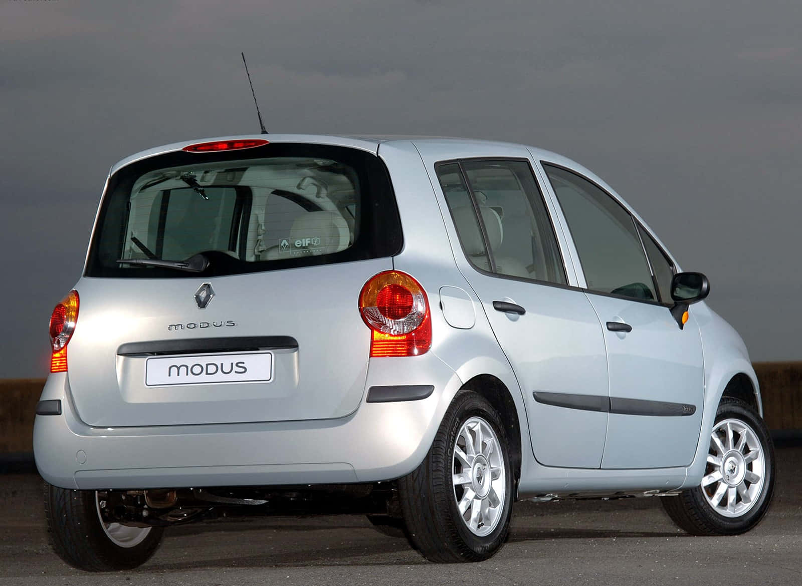 Renault Modus 桌布 壁紙 — 銀色雷諾Modus緊湊型車，從後方四分之三角度觀看，背景為多雲天空，位於鋪砌表面上。