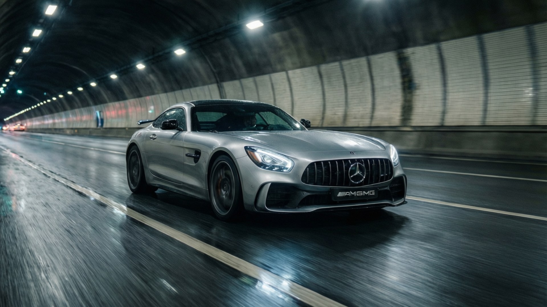 AMG GT Tunnel Speed 壁紙 — 一輛銀色 Mercedes AMG GT 跑車在潮濕的隧道中疾馳，燈光模糊，瀝青路面反射光線。
