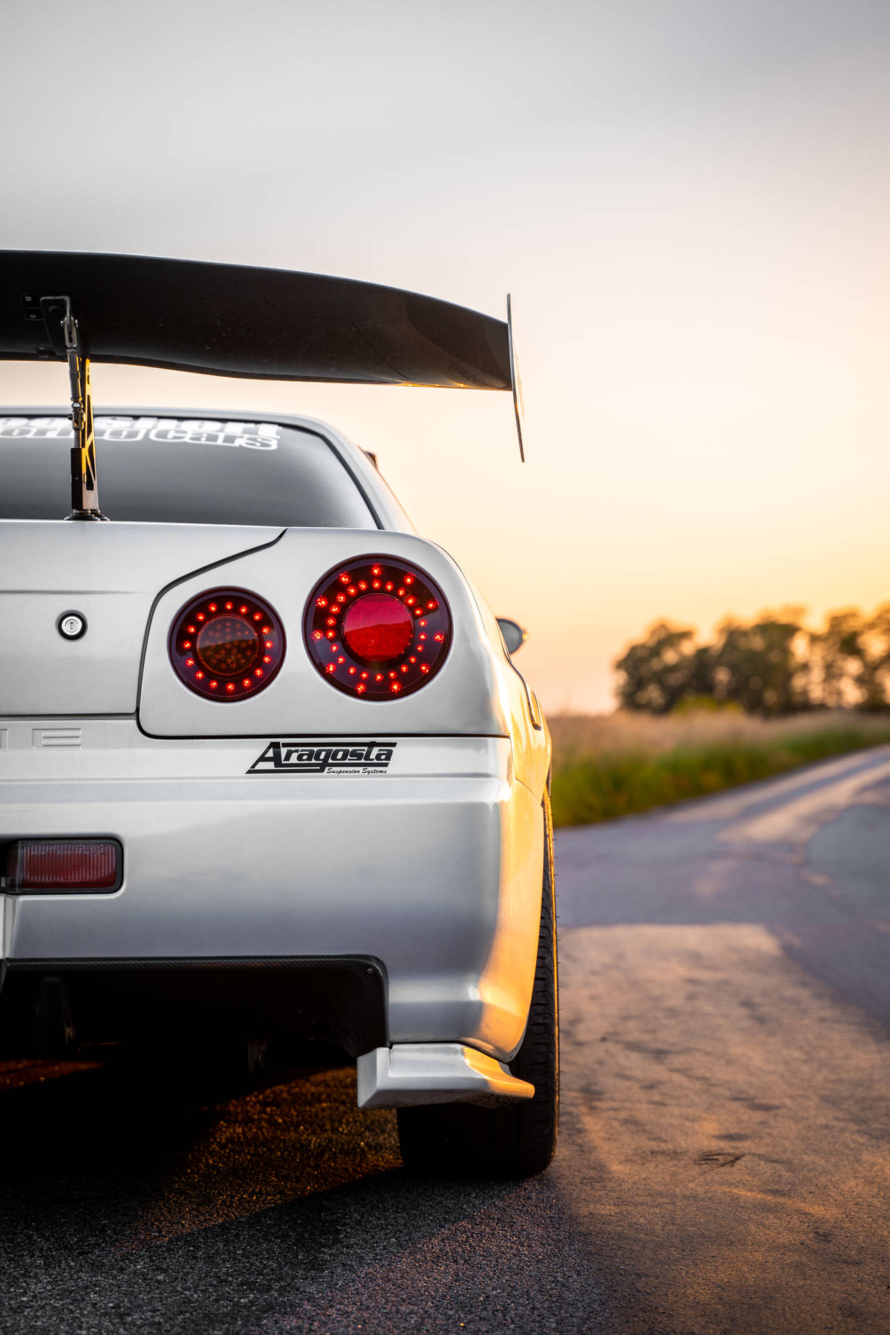 銀色日產GT-R，帶有紅色尾燈，停在日落時分的鄉村道路上。 — 天際線 壁紙