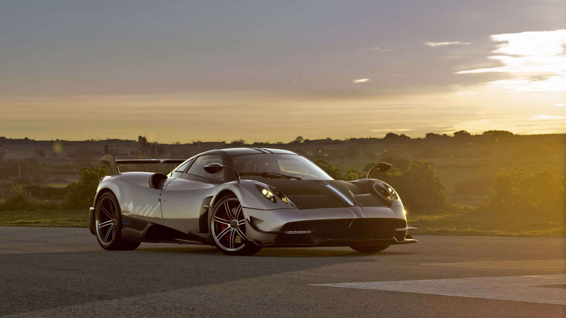  壁紙 — 一輛時尚的銀色帕加尼 Huayra 跑車在開闊的道路上，在金色夕陽下閃閃發光。