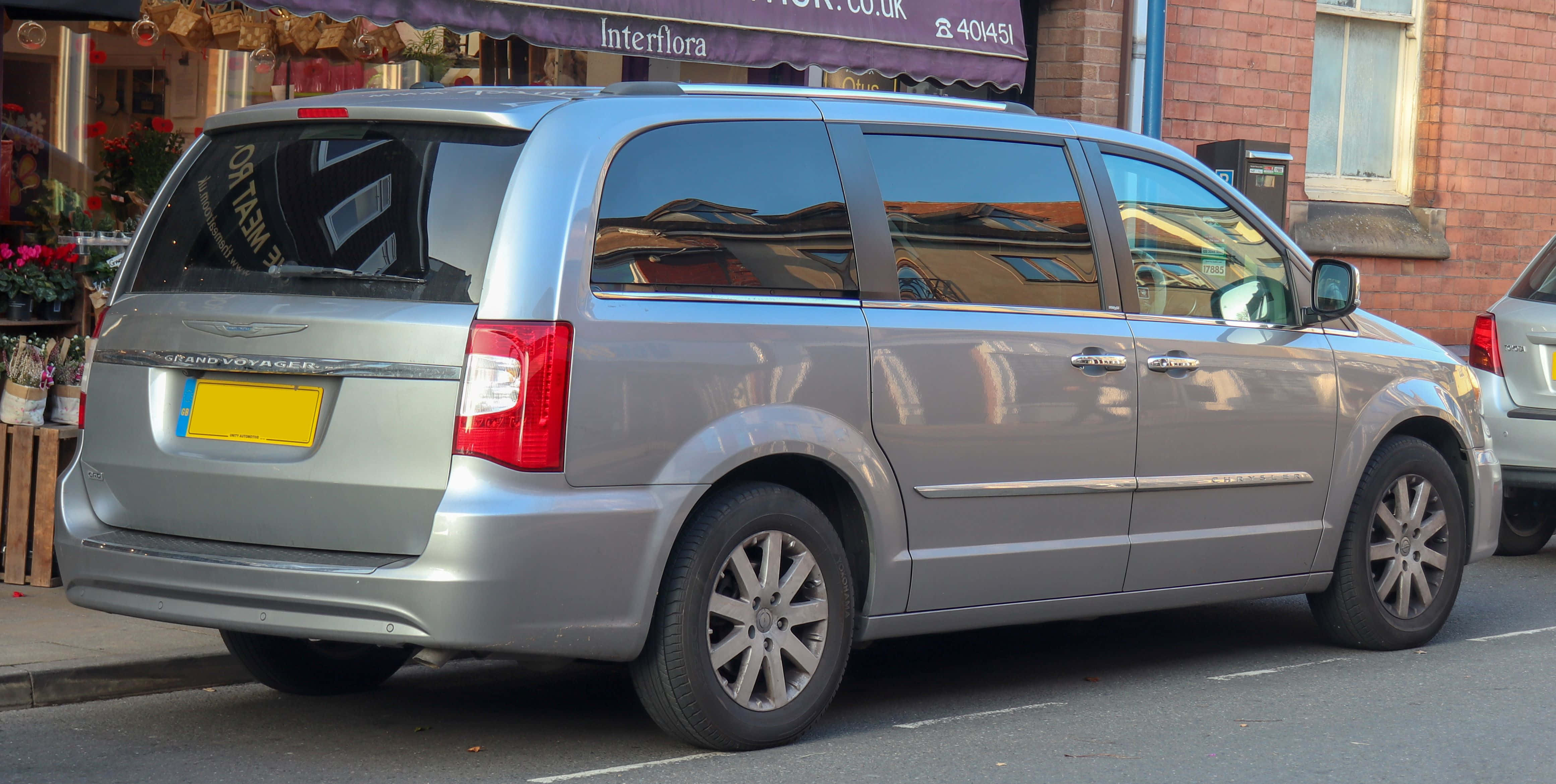 Chrysler Voyager 桌布 壁紙 — 銀色小型貨車停放在城市的街道上，旁邊是一棟帶有花店遮陽篷的磚砌建築。