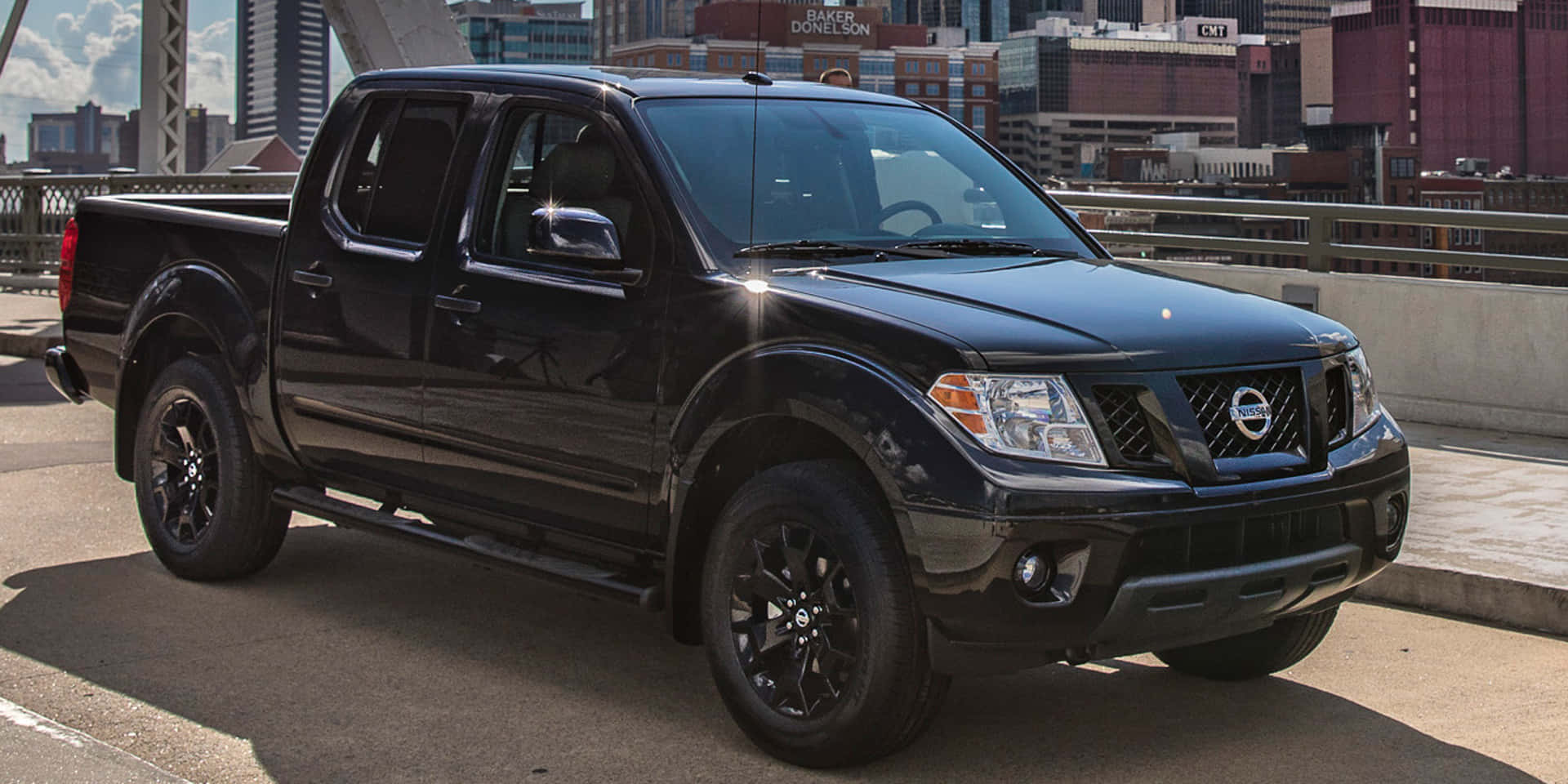 Nissan Frontier 桌布 壁紙 — 一輛亮黑色日產Frontier皮卡車停在城市橋樑上，背景是高樓大廈，在明亮的日光下。