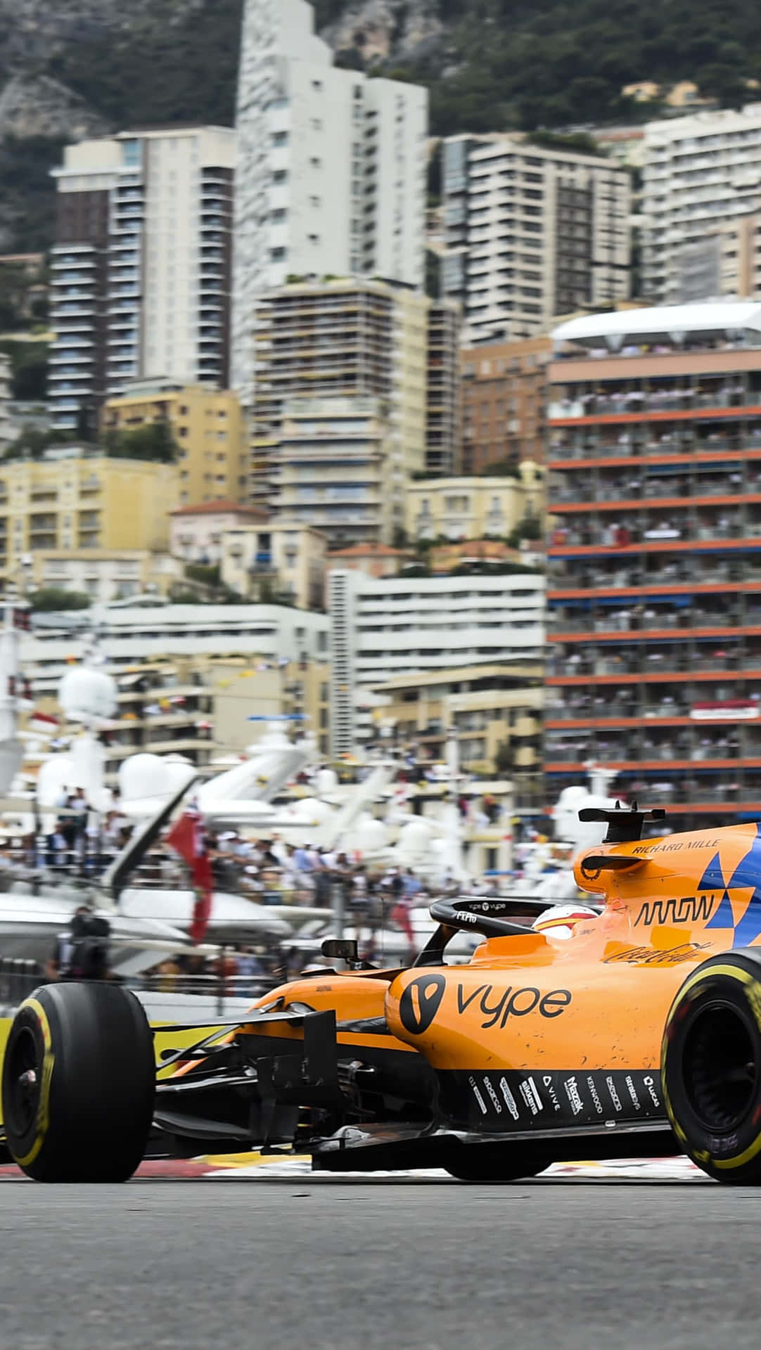 橙色一級方程式賽車在人群和建築物中飛馳經過摩納哥港。 — F1 壁紙