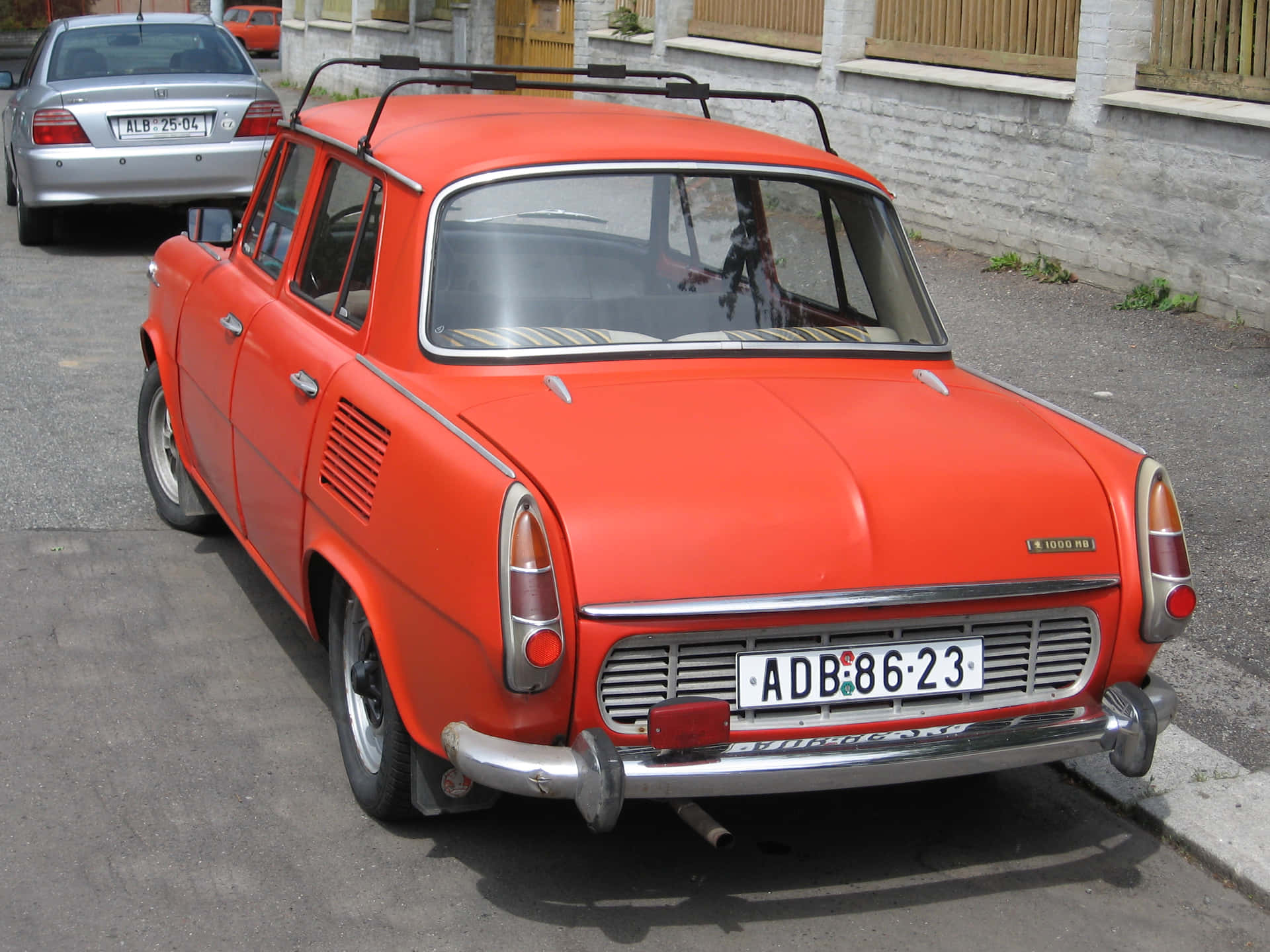  壁紙 — 一輛復古橙色 Trabant 汽車停放在鋪砌的街道上，旁邊是白色磚牆。
