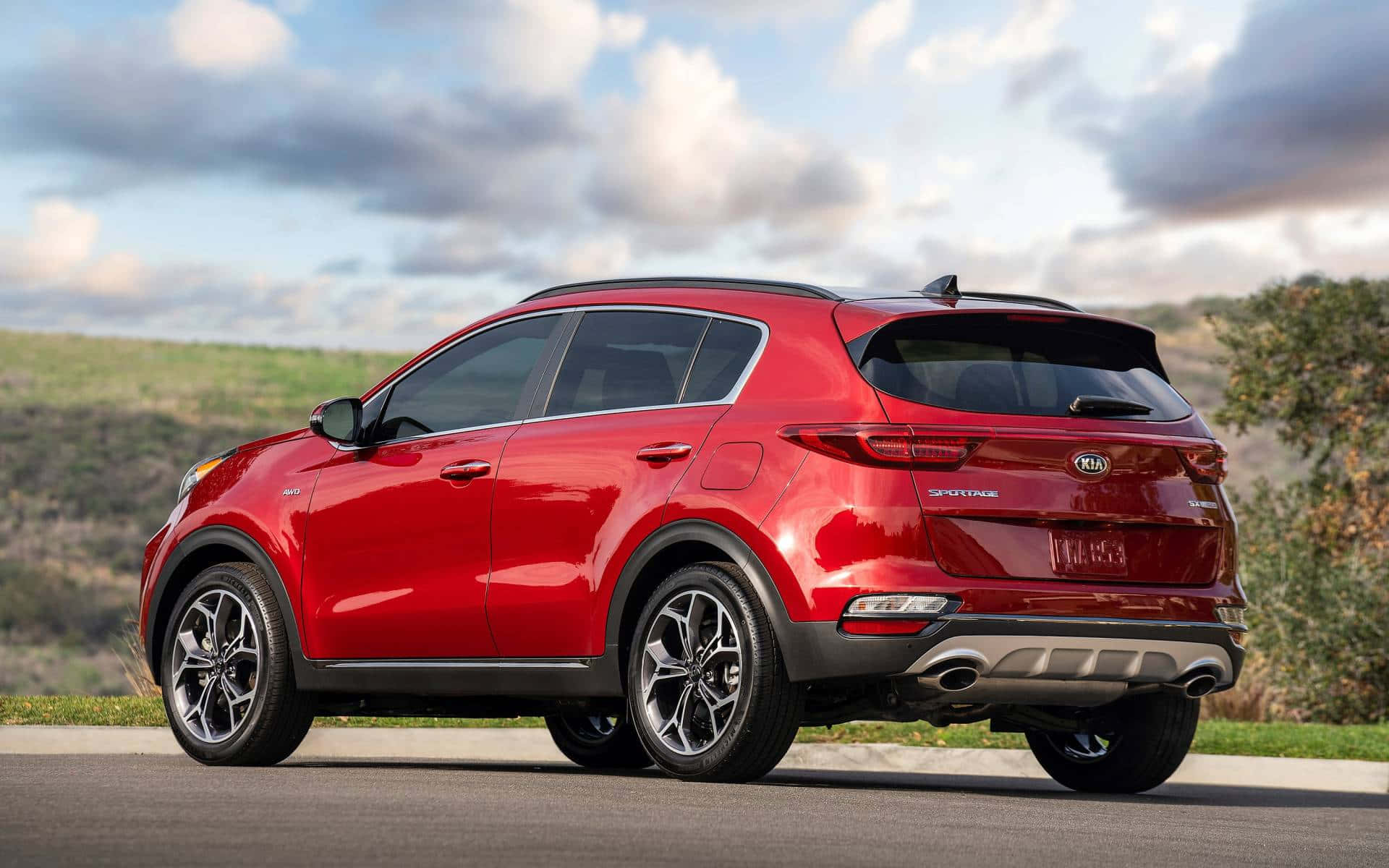 Kia Sportage 桌布 壁紙 — 一輛亮紅色Kia Sportage SUV停放在路邊，背景是起伏的丘陵和多雲的天空。