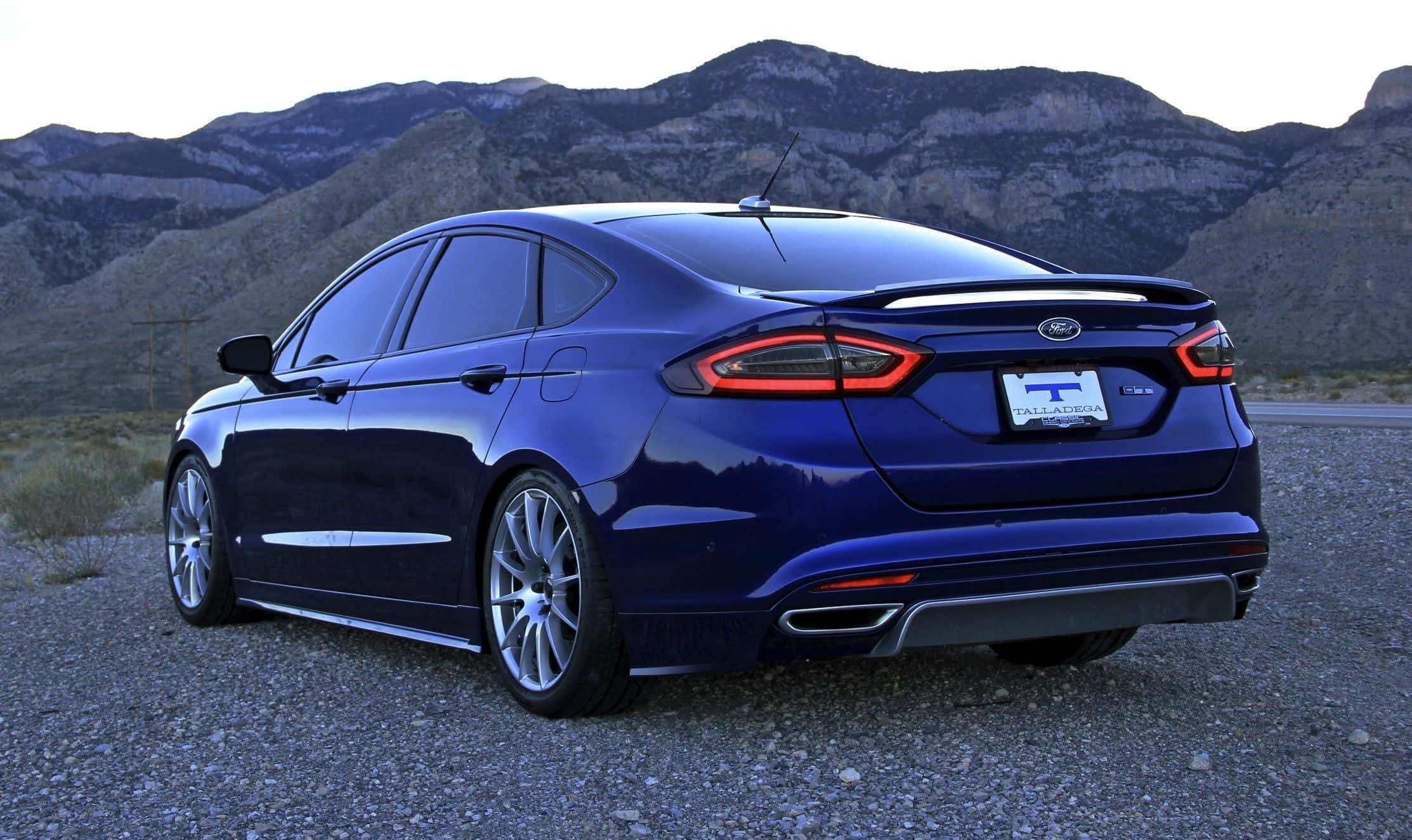 Ford Fusion 桌布 壁紙 — 一輛亮藍色福特Fusion房車停在碎石路上，背景是黃昏時崎嶇的山脈。