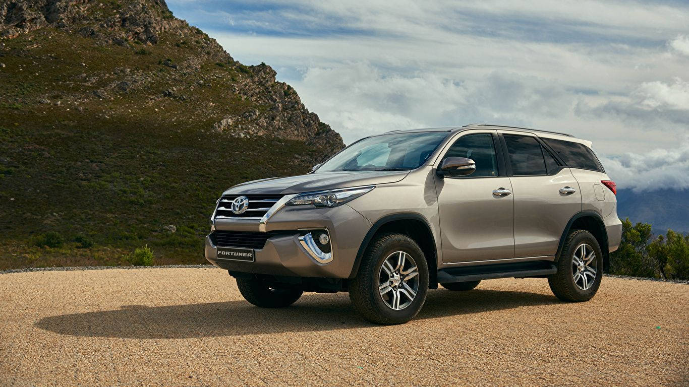 銀色豐田 Fortuner SUV 停泊在岩石地形和多雲天空的山路上。 — Toyota Supra 壁紙