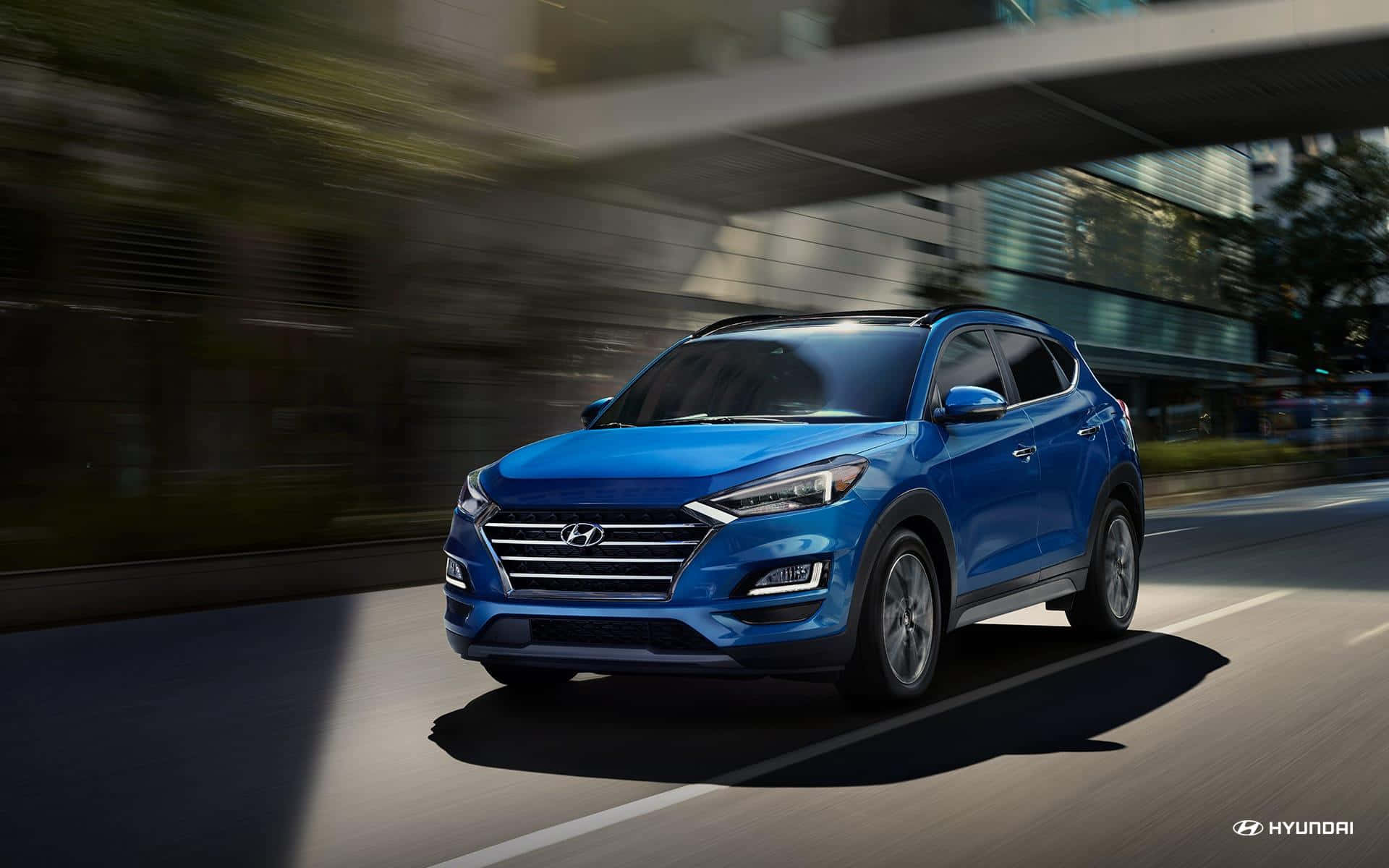 Hyundai Tucson 桌布 壁紙 — 一輛充滿活力的藍色現代 Tucson SUV 在現代城市街道上行駛，背景呈現動態模糊效果。