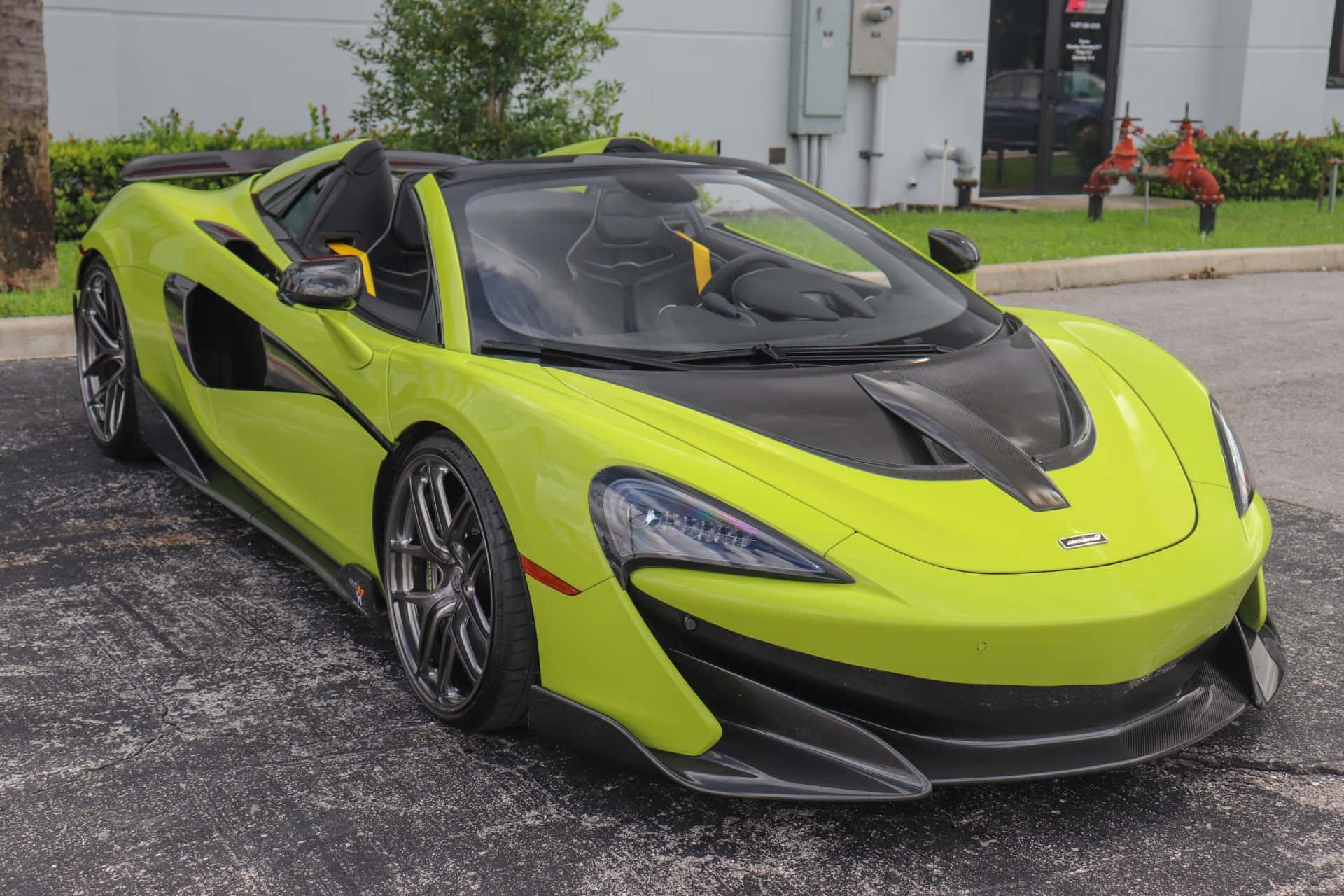 Mclaren 600lt Spider 桌布 壁紙 — 一輛充滿活力的萊姆綠色McLaren跑車，帶有黑色飾邊，停放在建築物和綠化附近的柏油路面上。