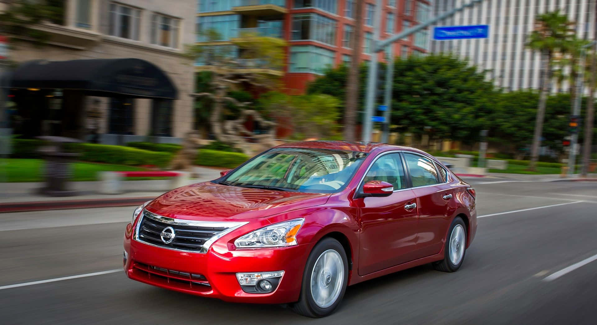 Nissan Altima 桌布 壁紙 — 一輛鮮紅色轎車在陽光明媚的城市街道上飛馳，背景是模糊的建築物和棕櫚樹。