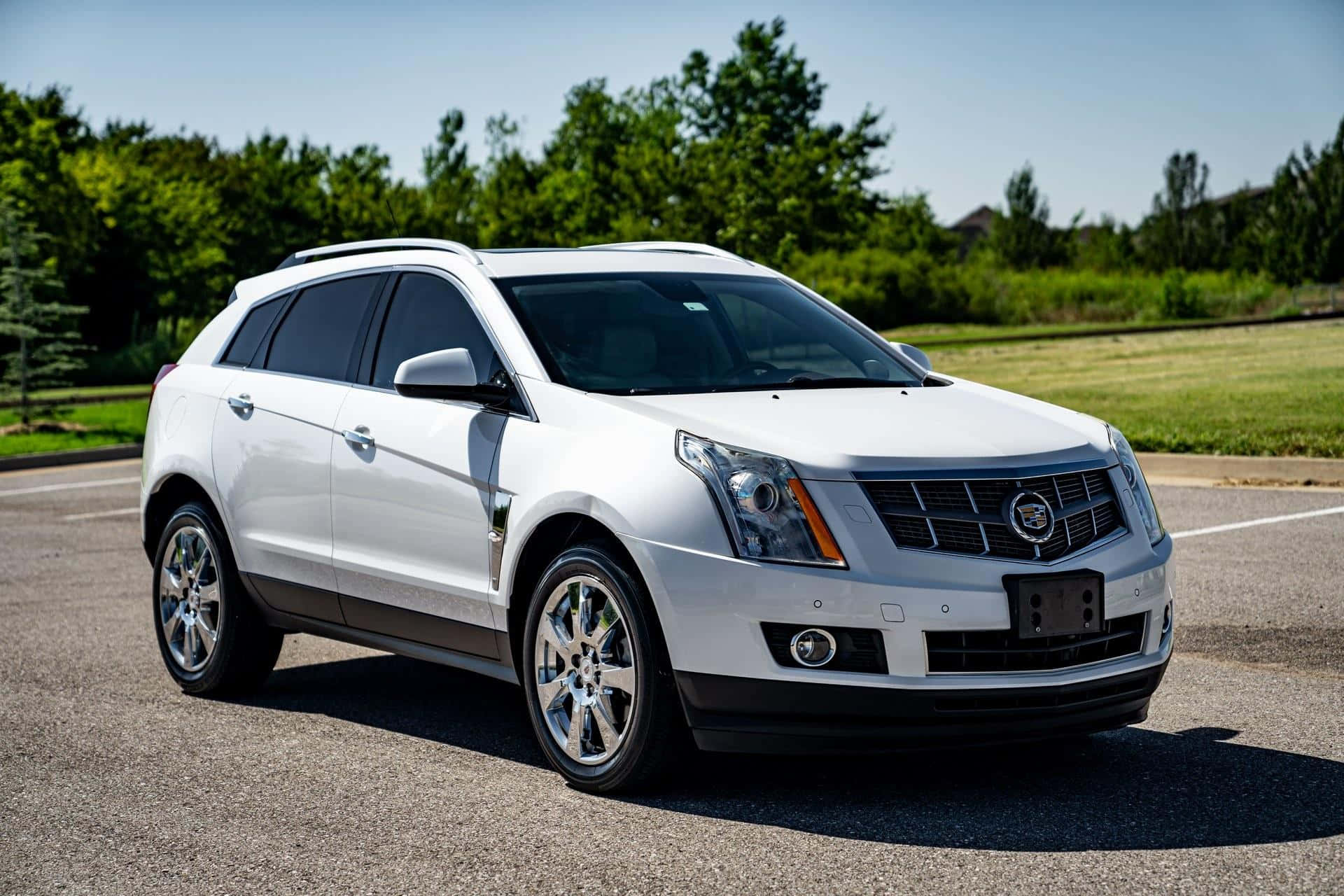 Cadillac Srx 桌布 壁紙 — 一輛純白色的 Cadillac SRX SUV 停泊在柏油路上，周圍有茂密的綠樹和草地，天空湛藍清澈。