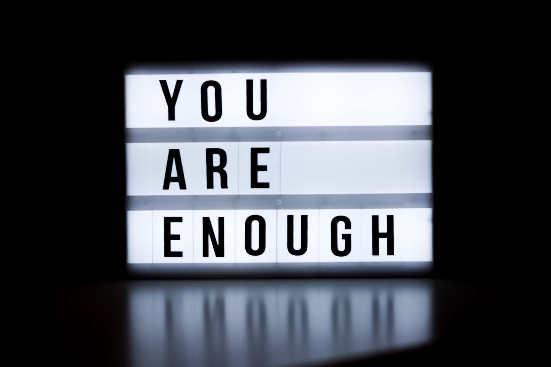 壁紙 — 一個發光的燈箱在純黑背景上以粗體黑色字母顯示「YOU ARE ENOUGH」訊息。