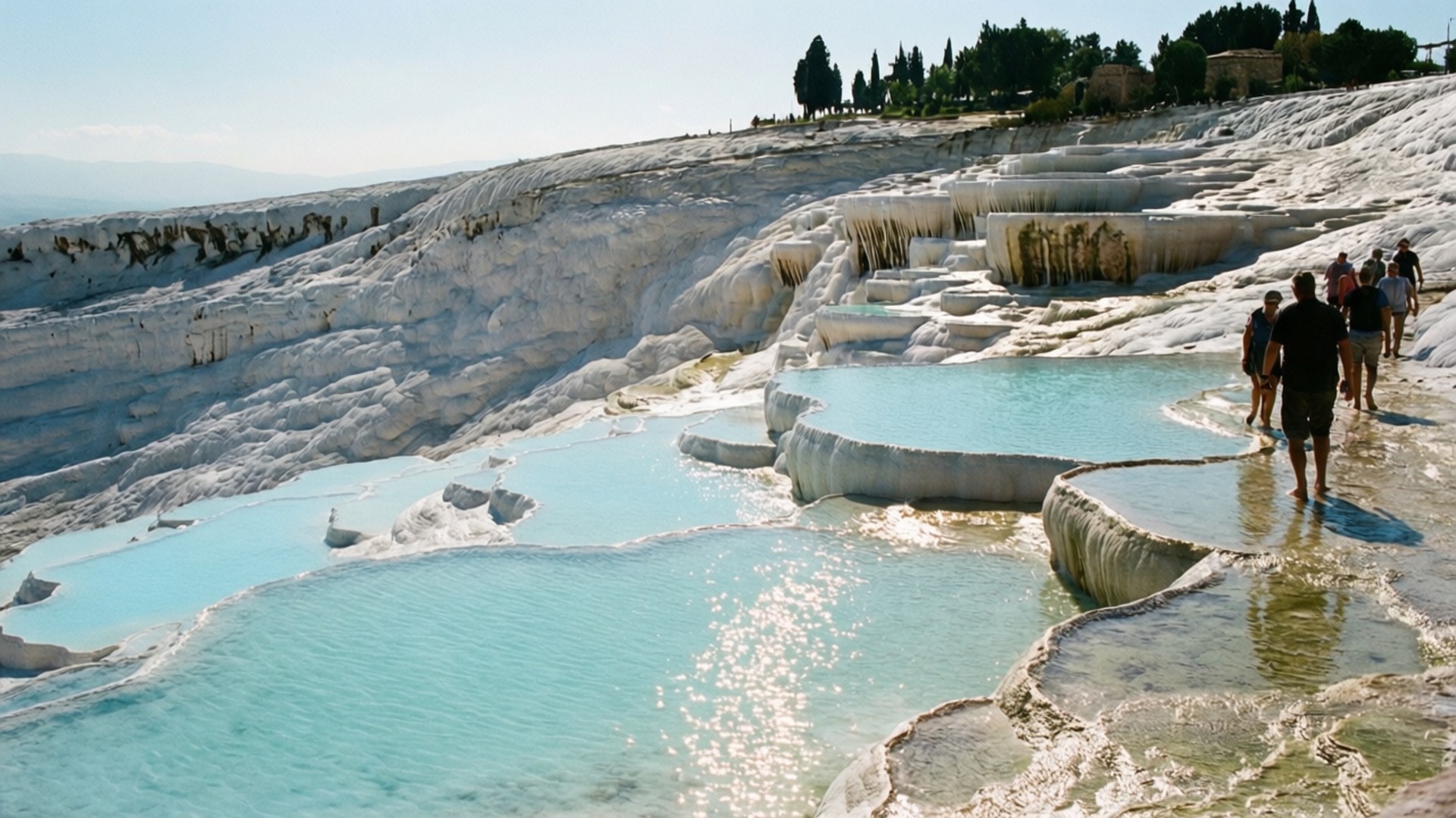 Pamukkale Thermal Pools 壁紙 — 遊客在晴朗的藍天下，沿著被白色礦物 formations 包圍的梯田式碧綠水池漫步。