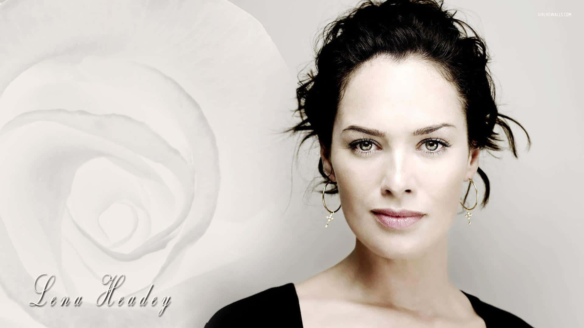 Lena Headey 桌布 壁紙 — 一位優雅的黑髮女性戴著金色耳環，在柔和的白玫瑰背景前凝視前方。