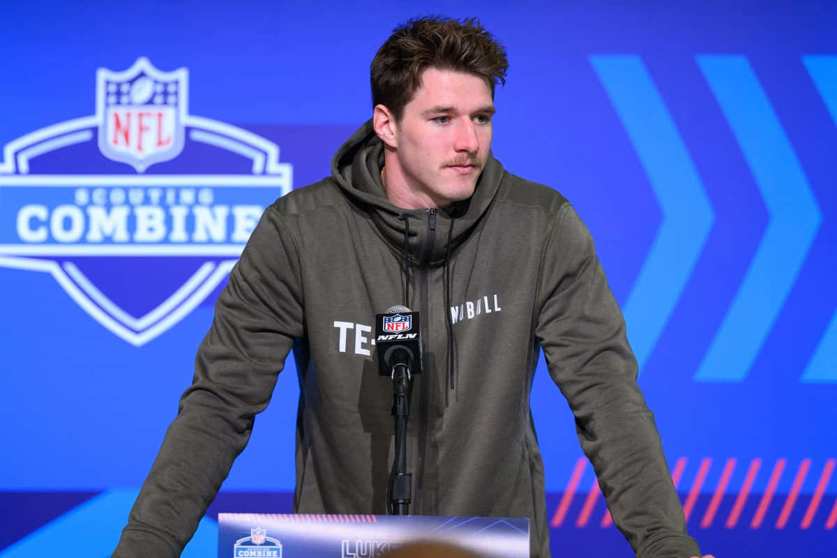  壁紙 — 一位身穿灰色連帽衫的年輕足球員在NFL選秀聯合試訓記者會上站在講台上。