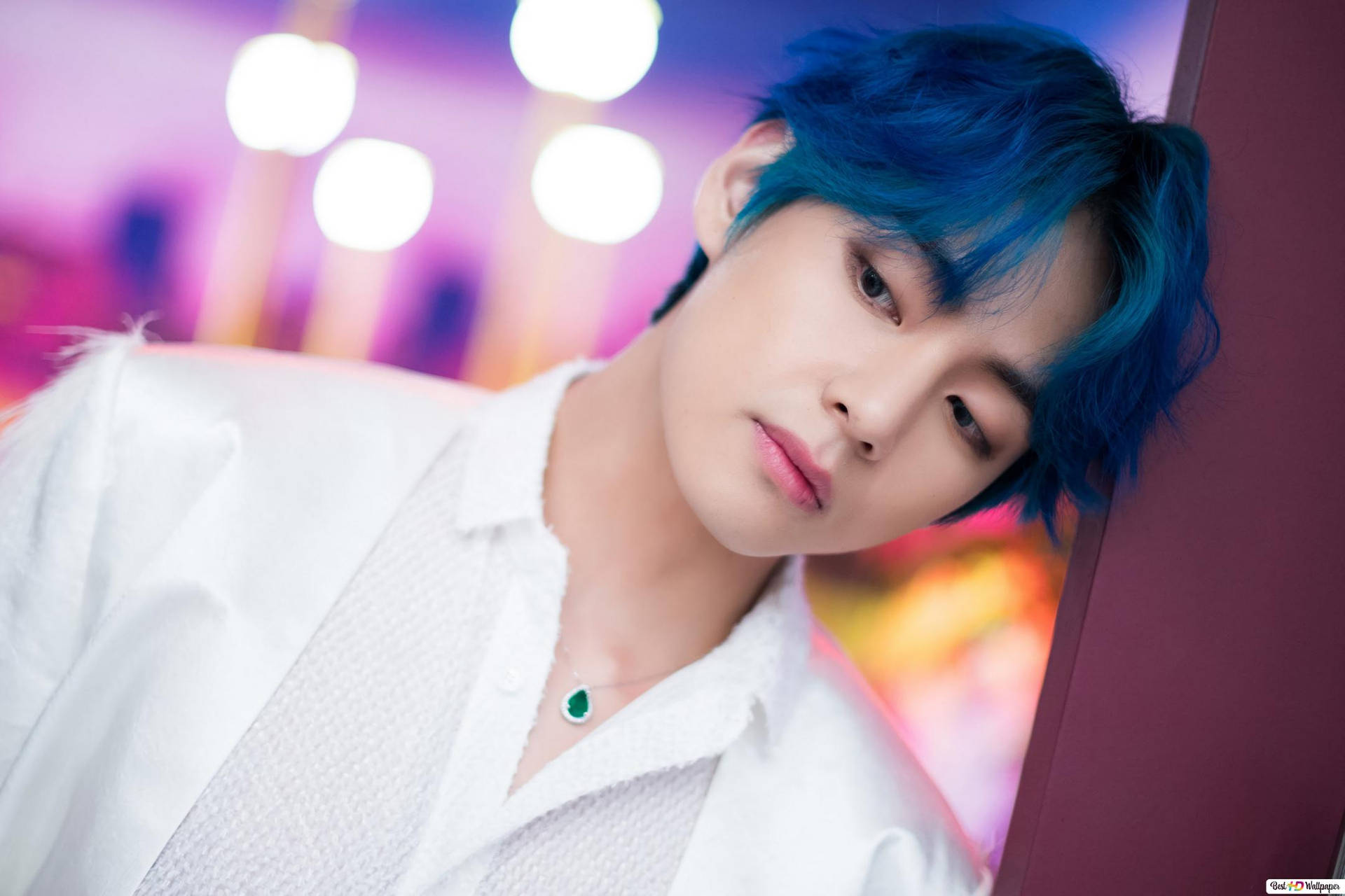 藍髮年輕男子穿著白色襯衫和綠色項鍊，在發光的燈光前。 — K Pop 壁紙