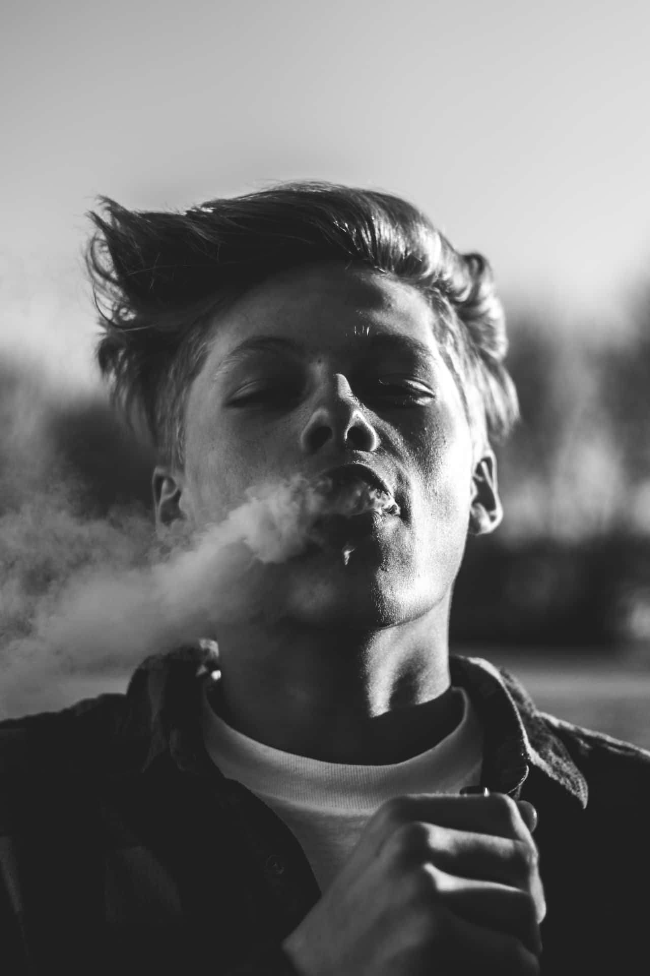  壁紙 — 一個年輕男子在戲劇性的黑白肖像中呼出煙霧，風吹亂了他的頭髮。