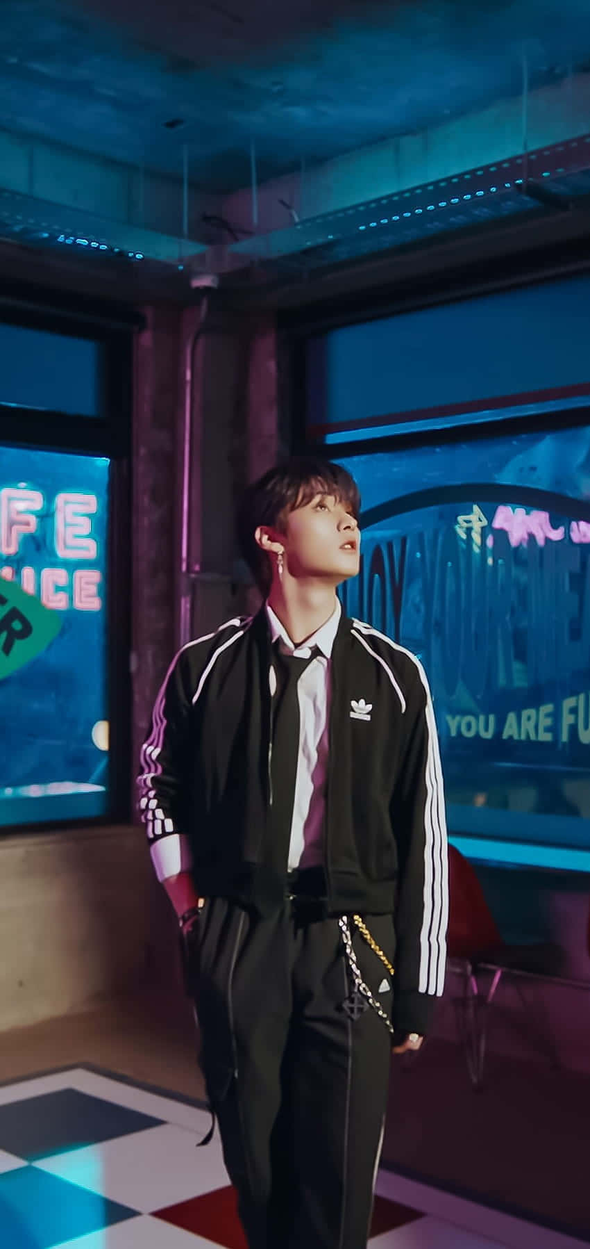  壁紙 — 一名身穿黑色Adidas運動服的年輕男子站在一個霓虹燈照亮的城市風格房間內，地板是棋盤格紋，還有發光的招牌。