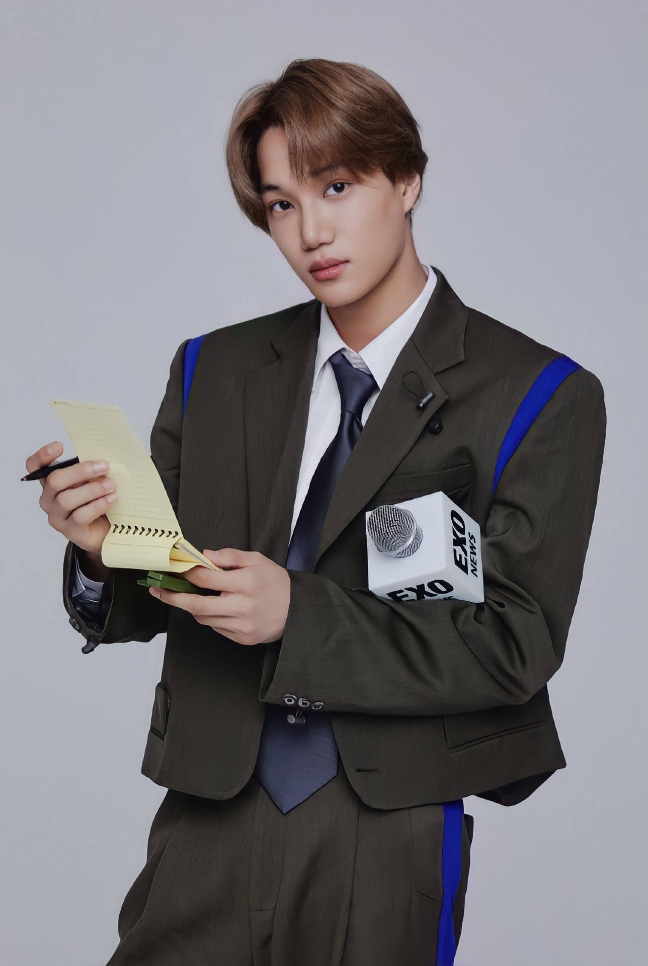 年輕男子身穿棕色西裝，手持筆記本和筆，手臂上有麥克風 — Exo 壁紙