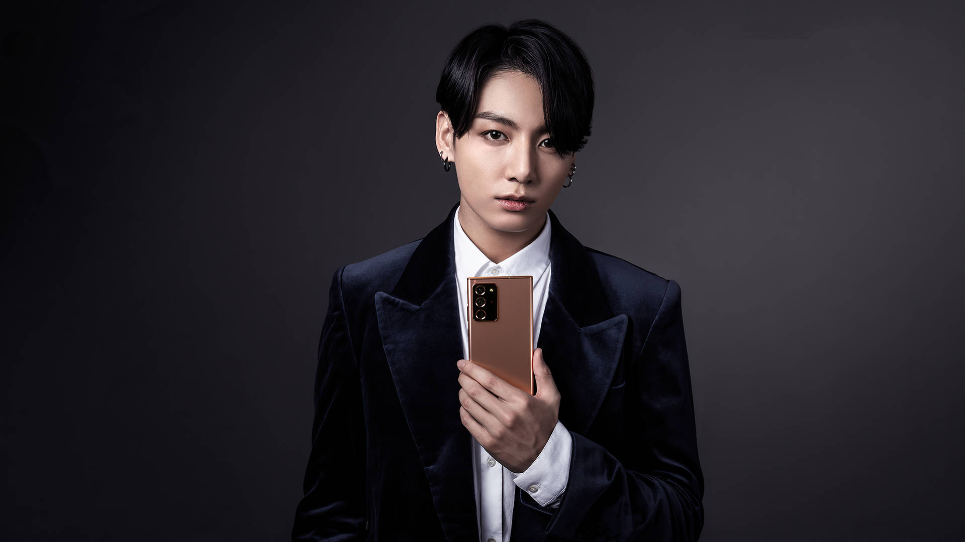 身穿天鵝絨西裝的男子在工作室肖像中手持玫瑰金手機 — Jungkook 壁紙